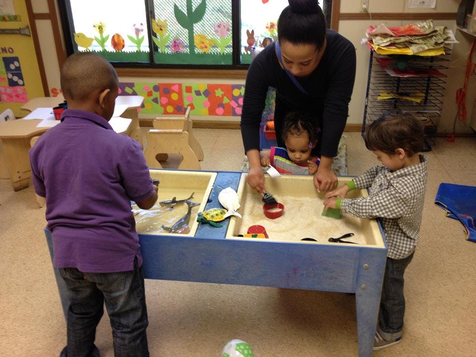 Adult and two children playing at a sand table in a classroom