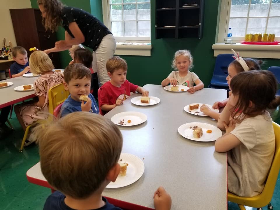 Children eating cake at a table with an adult in the background