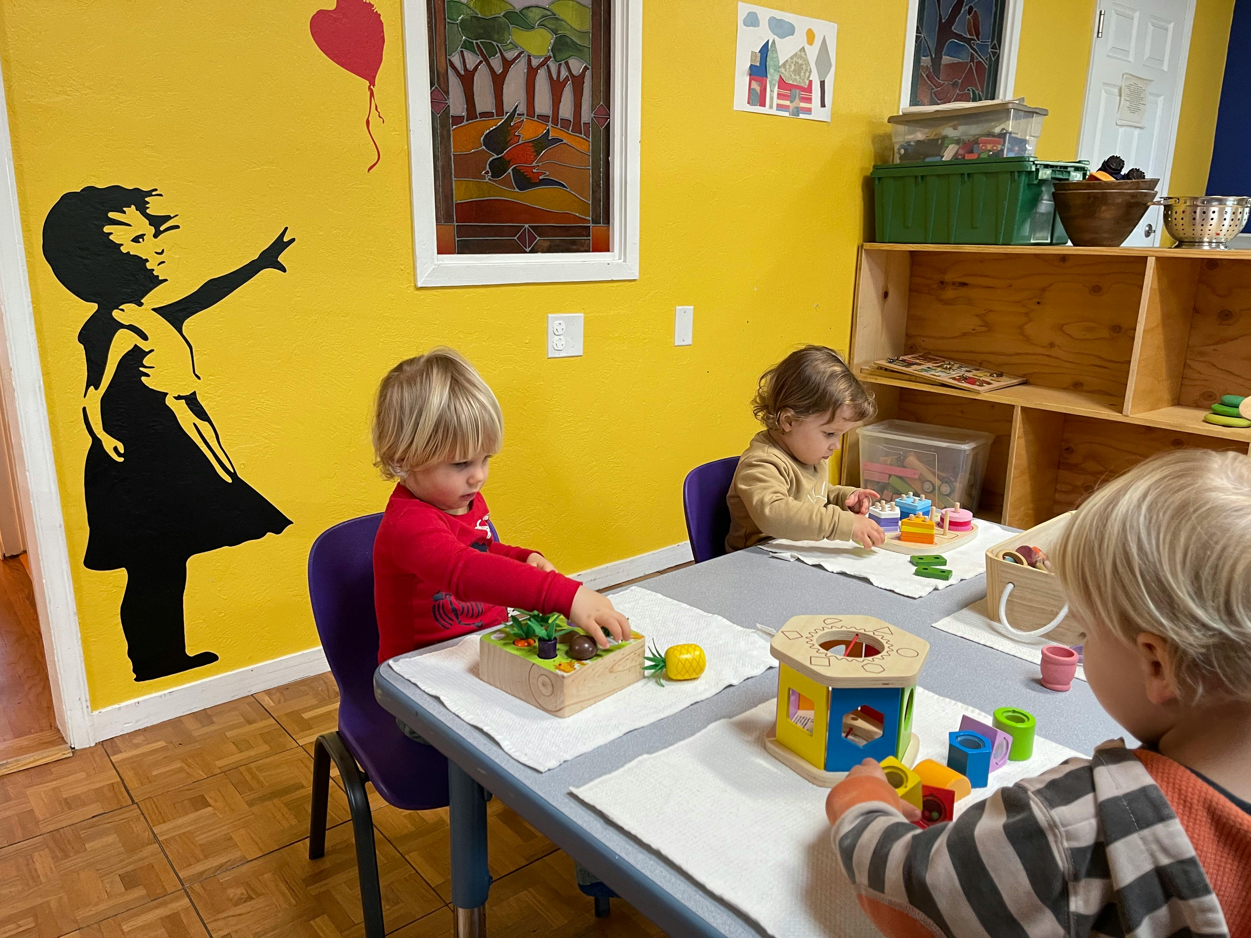 Three children playing with toys at a table in a classroom