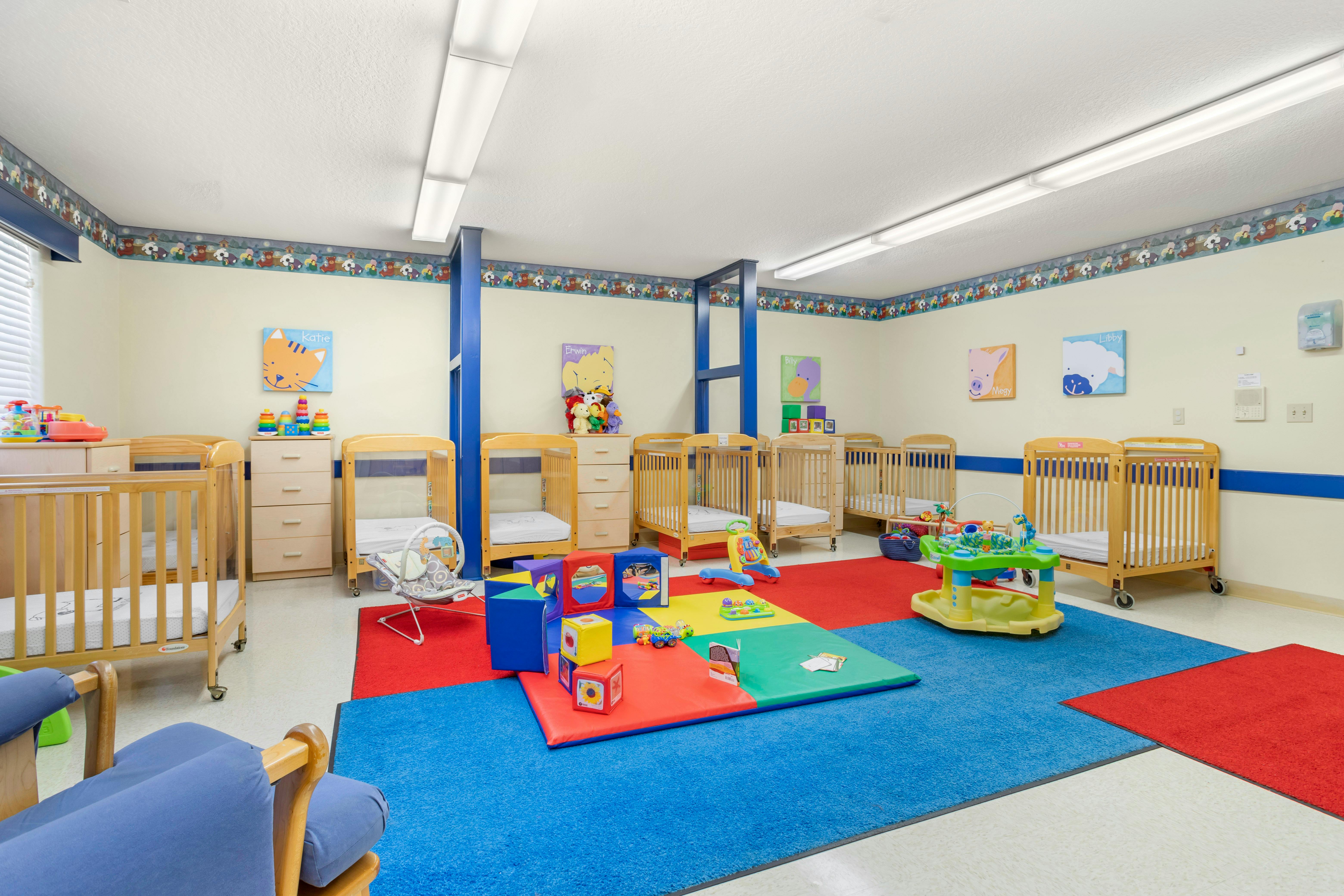 Baby room with several cribs, colorful playmats, and toys