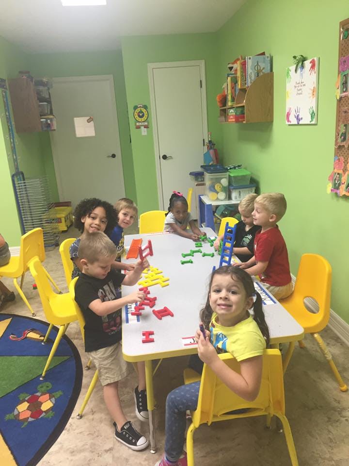 Children playing with colorful building blocks at a table in a classroom