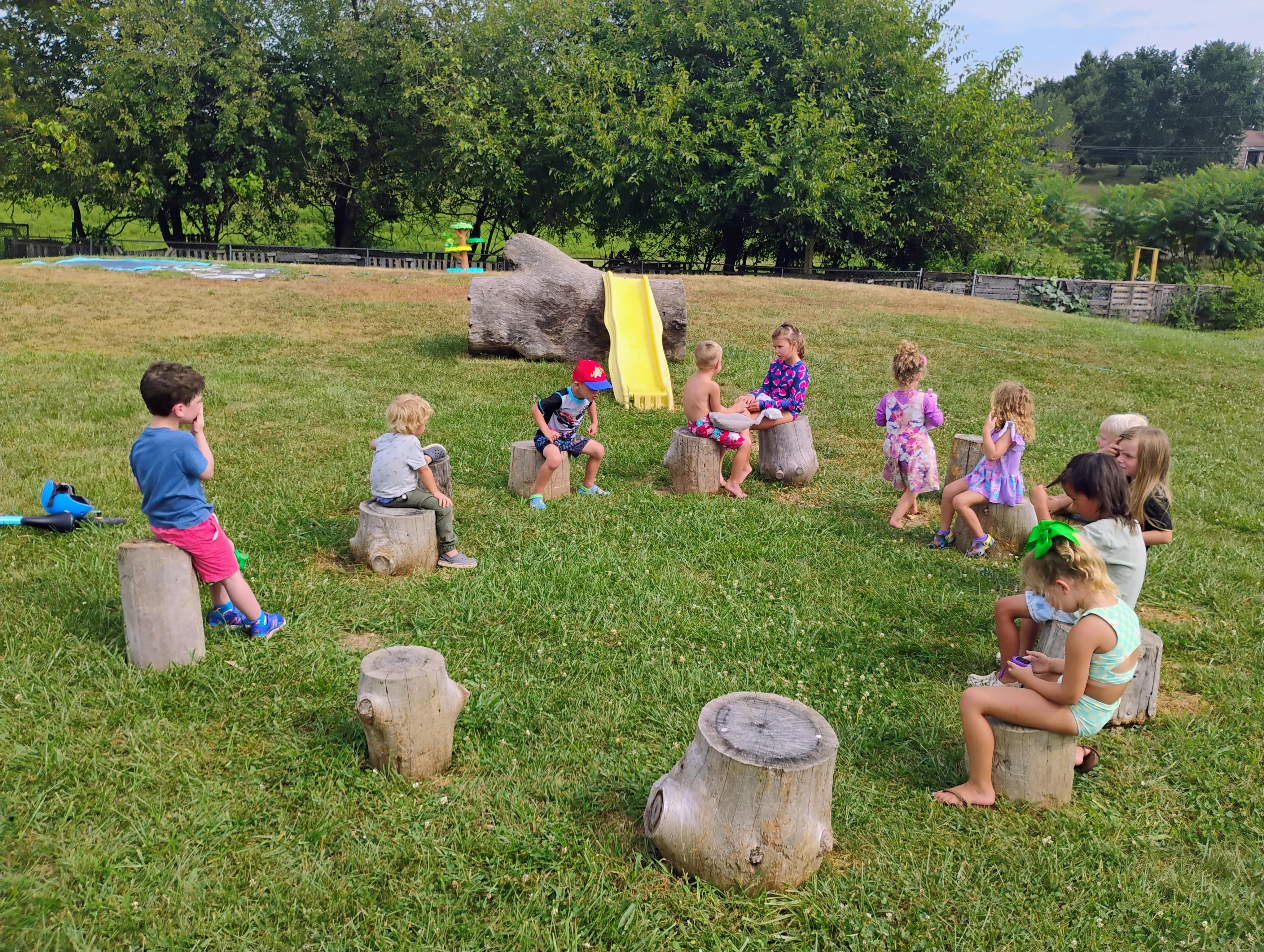 Children sitting on tree stumps in a circle outdoors