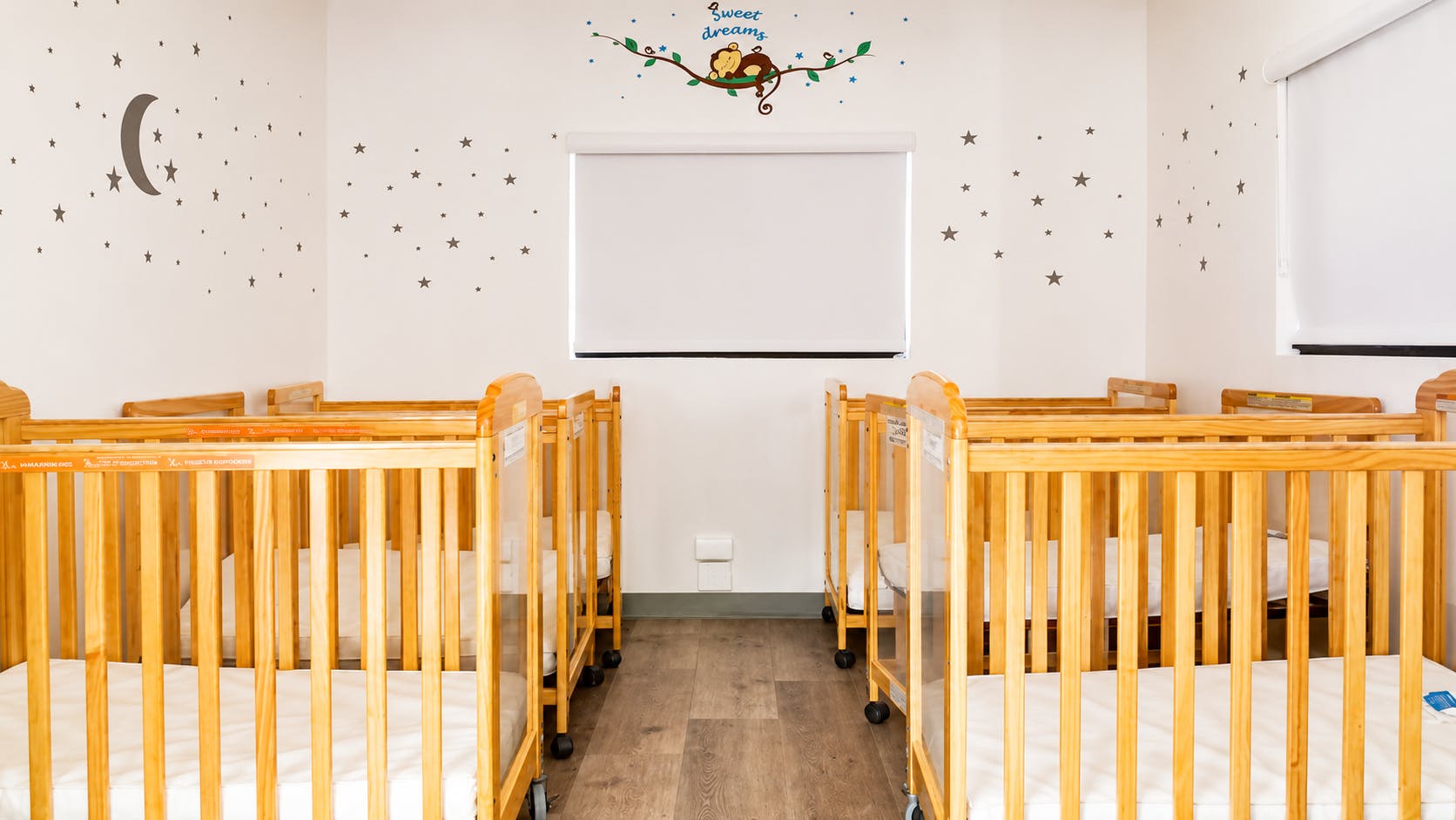 Several wooden cribs arranged in a nursery with star wall decals