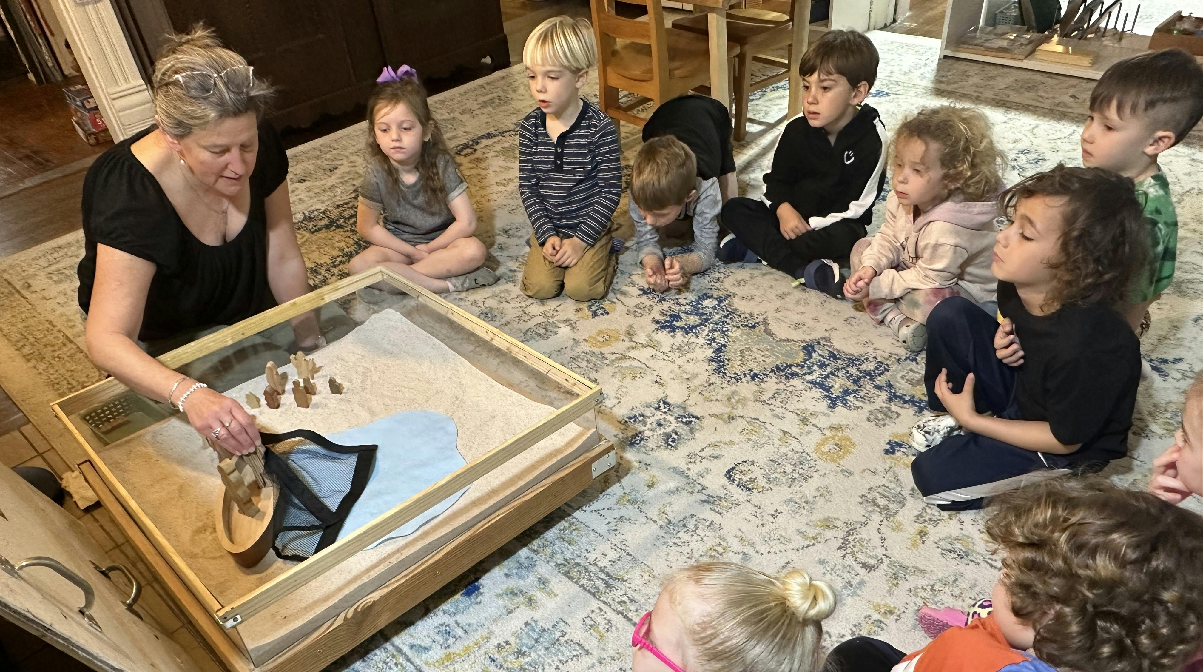 Adult and several children gathered around a sand-filled display case