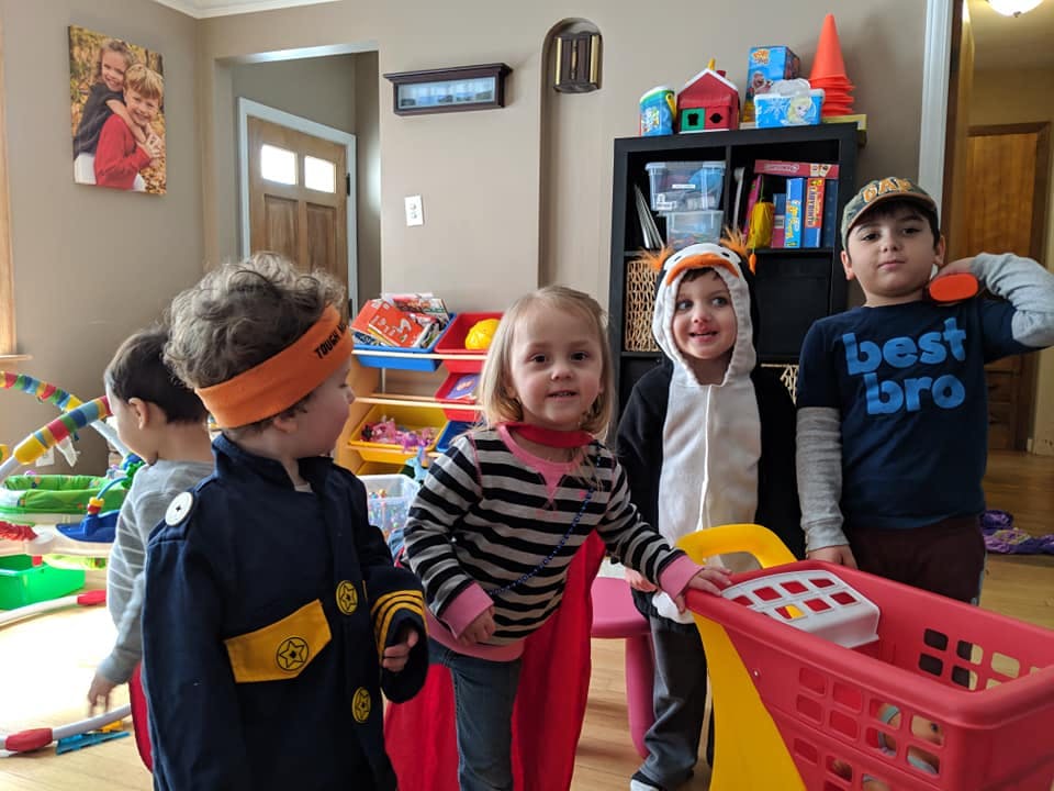 Four children in a room, one in a firefighter costume, one in a penguin costume