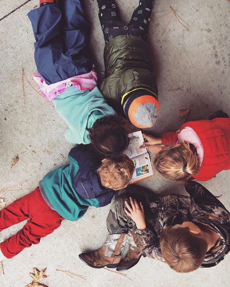 Four children lying on the ground looking at a book