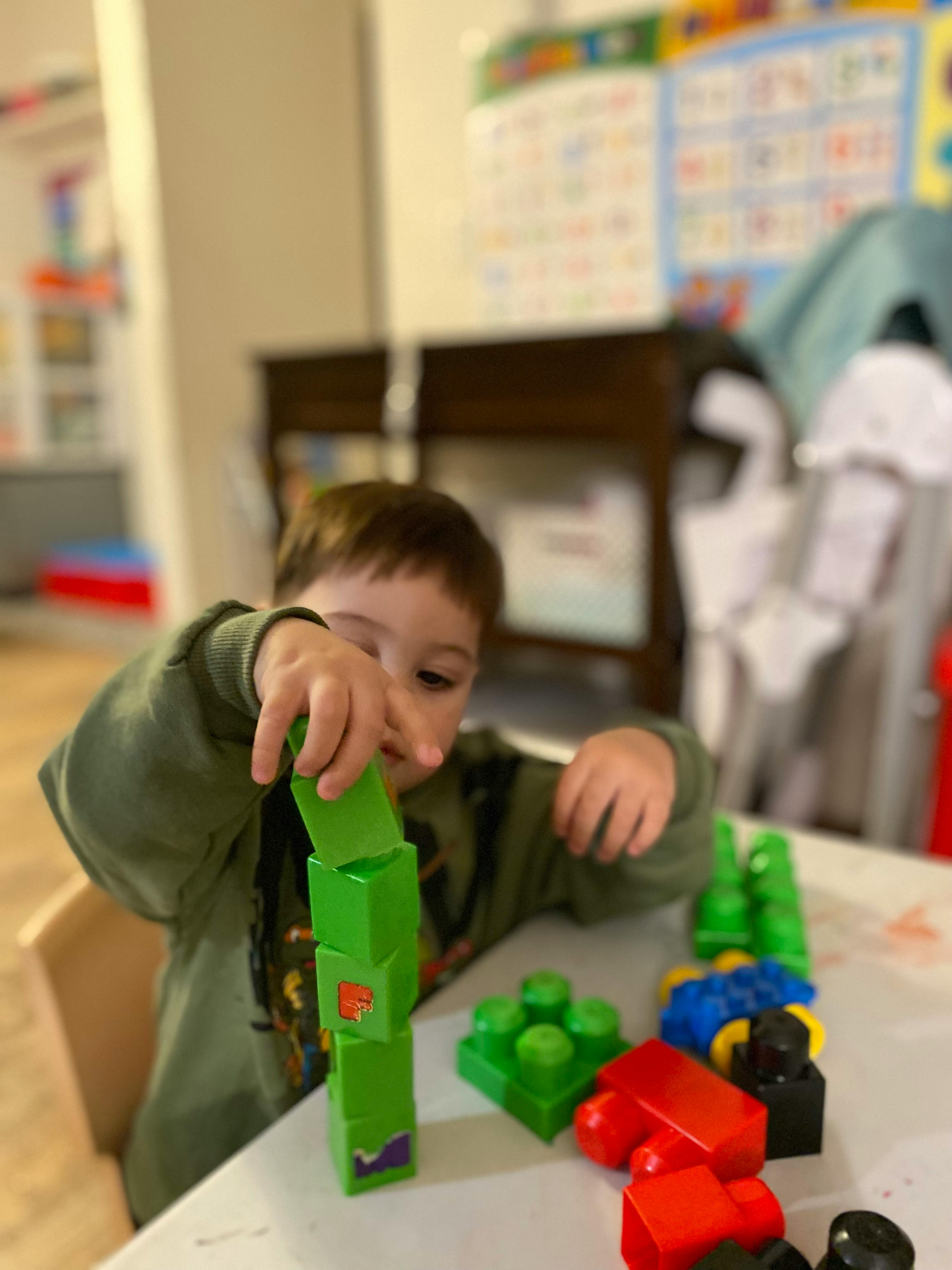 Child stacking green building blocks on a table