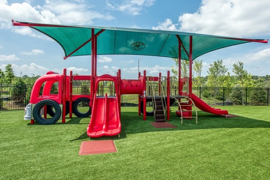 Red playground structure with slides and climbing areas under a teal shade
