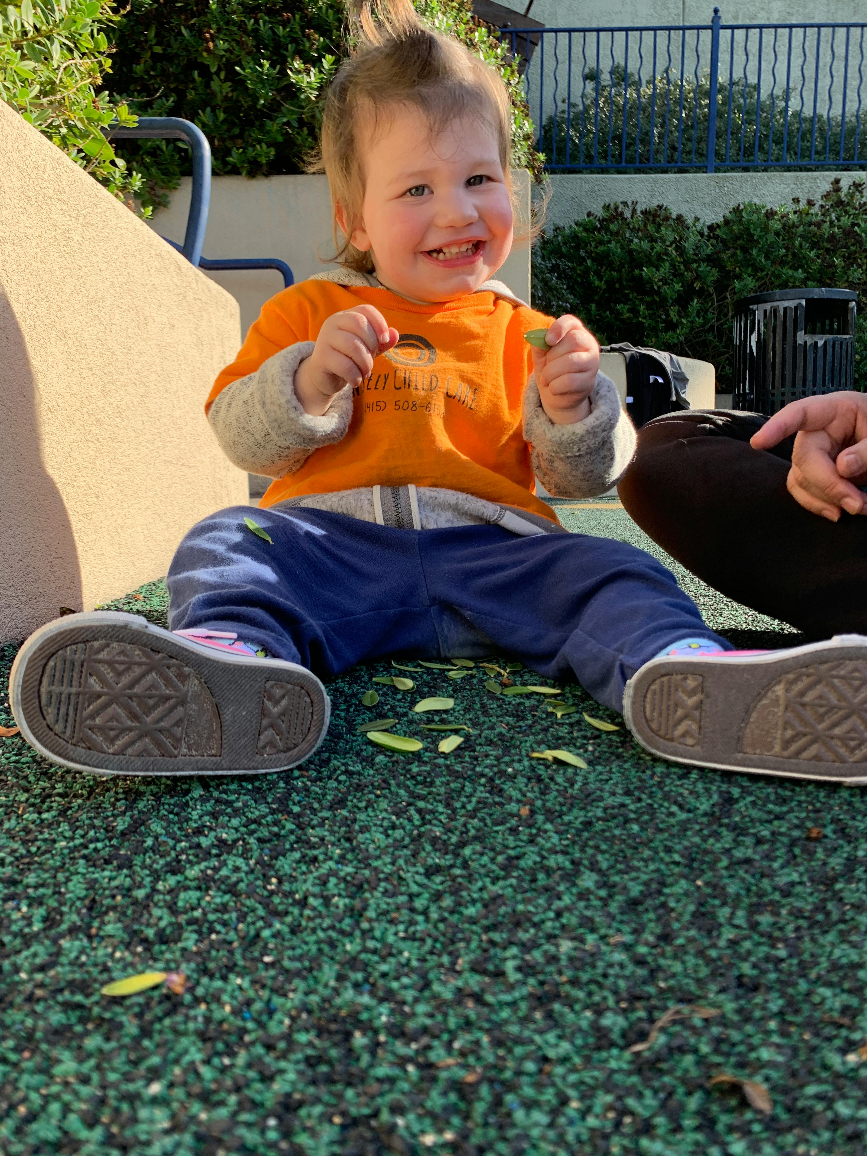 Child sitting on green ground holding small leaves