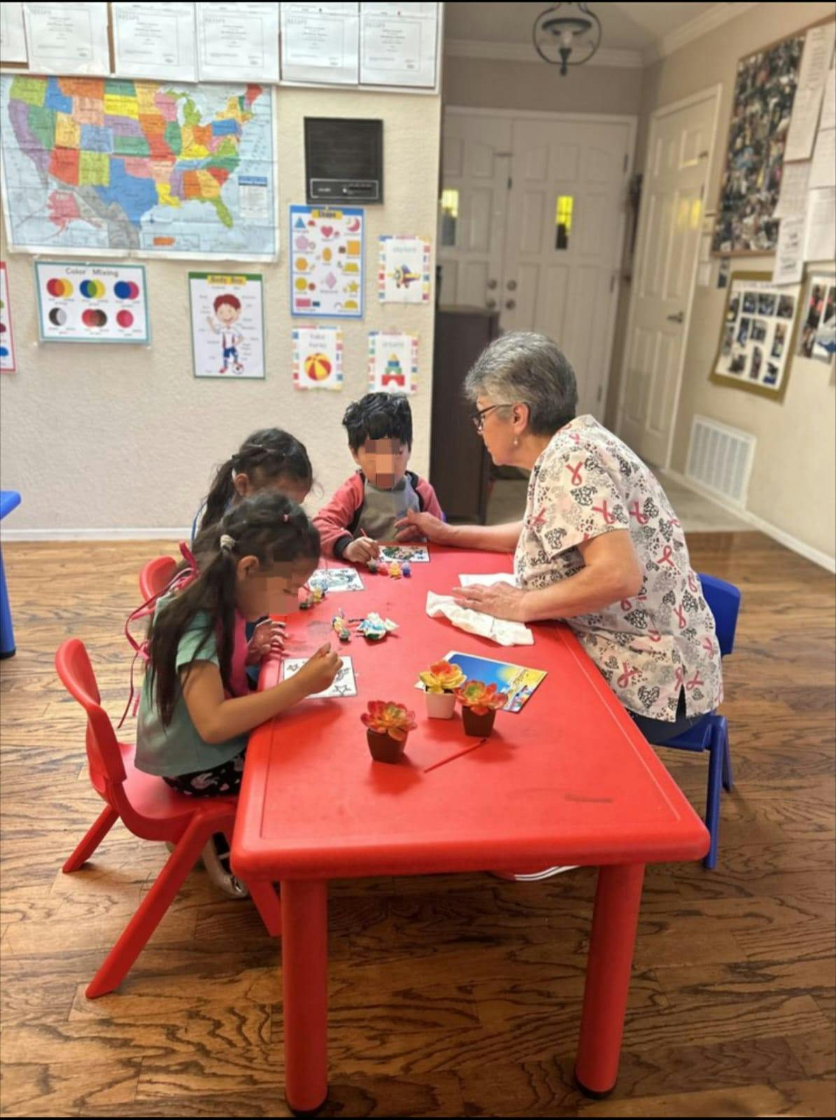 Adult and three children at a red table in a classroom