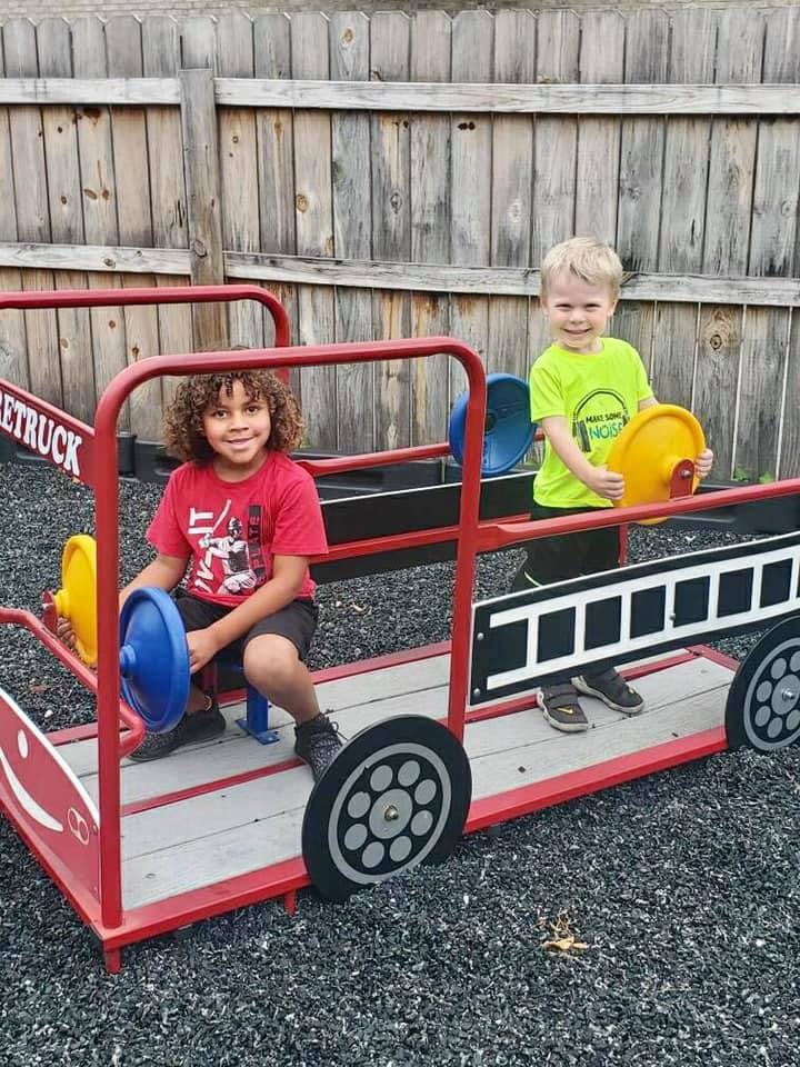Two children playing on a fire truck playground structure