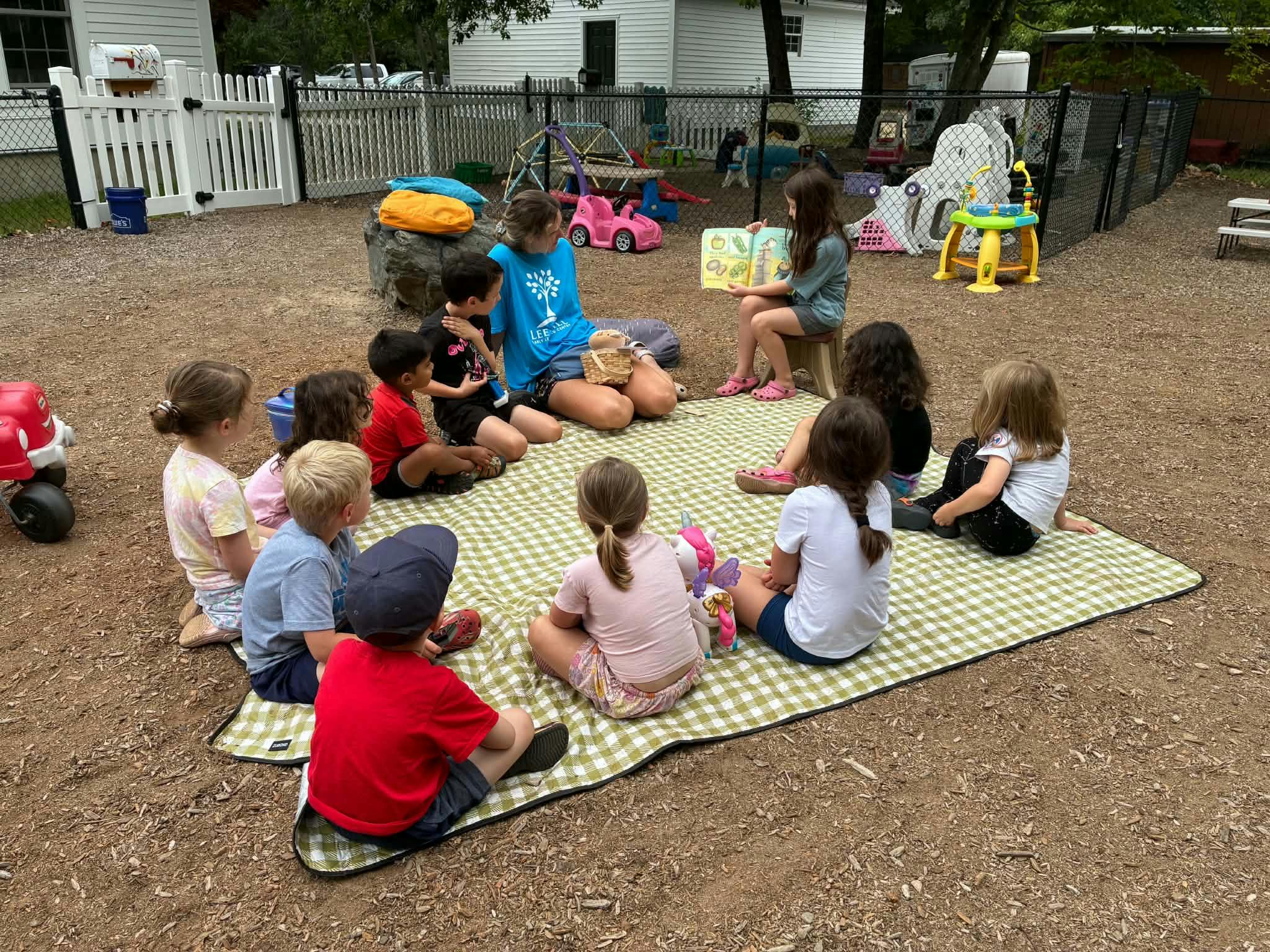 Group of children sitting on a blanket listening to a person reading a book