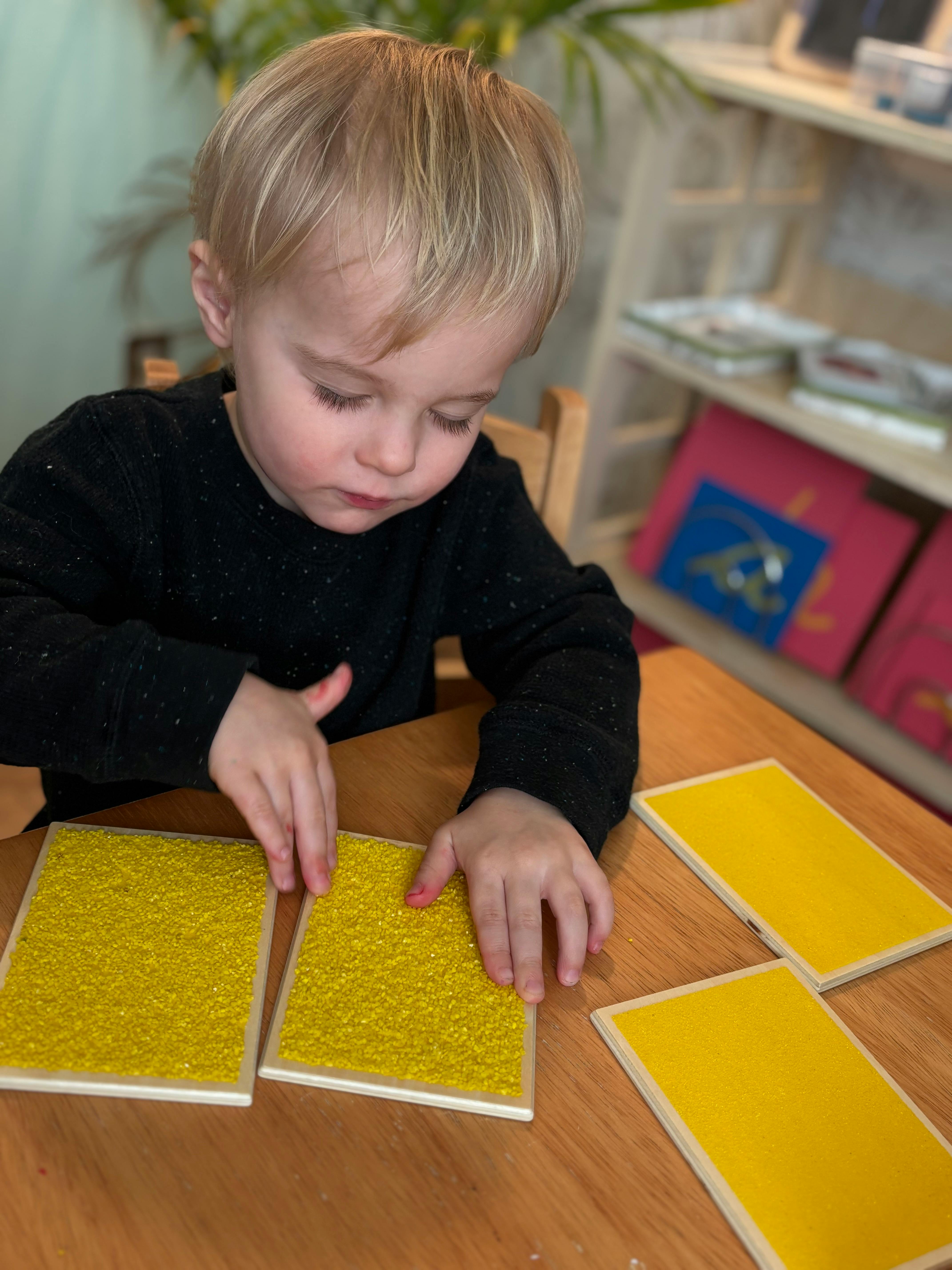Child touching yellow textured and smooth rectangular blocks on a table