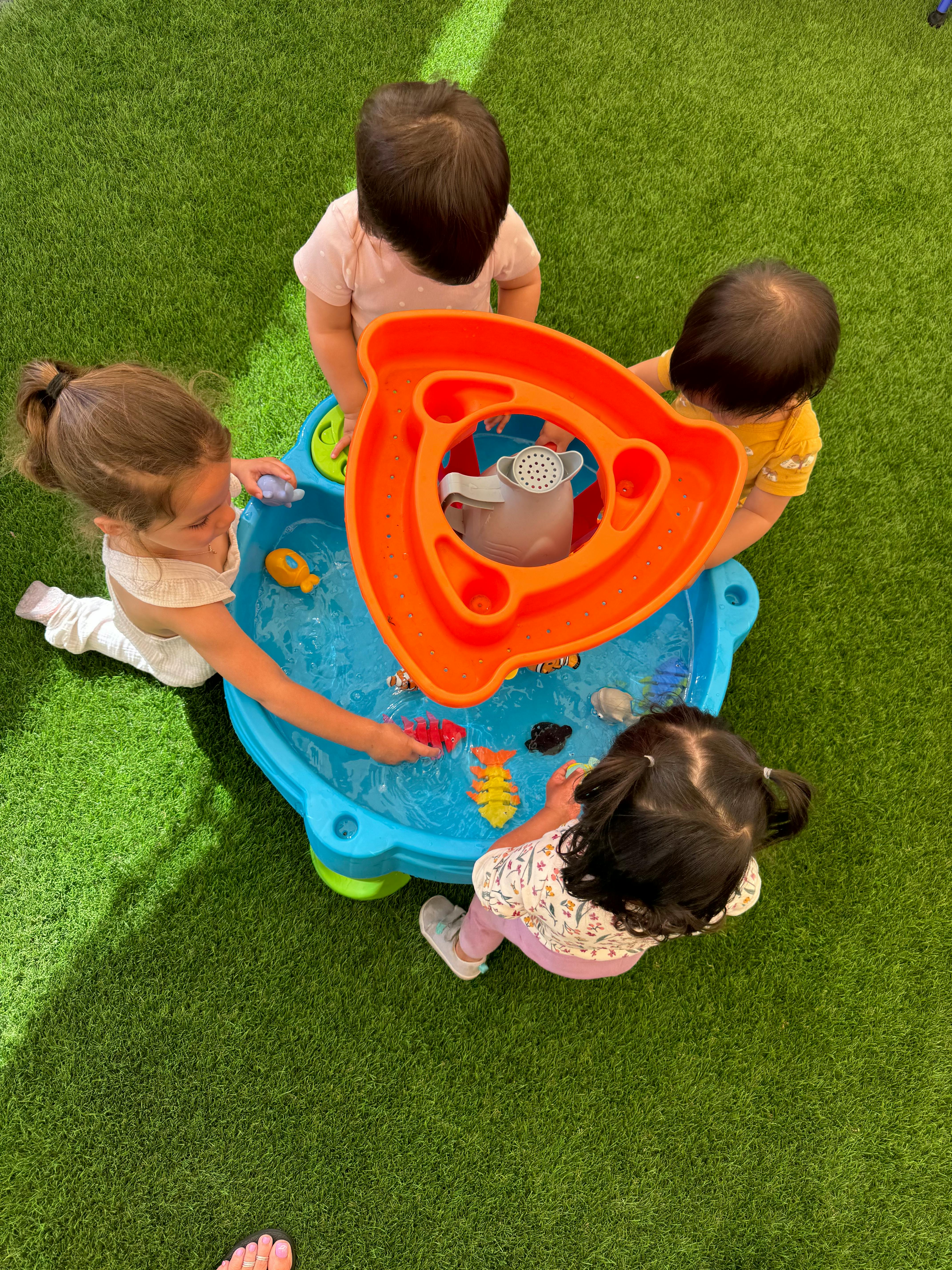 Four children playing with a water table on green grass