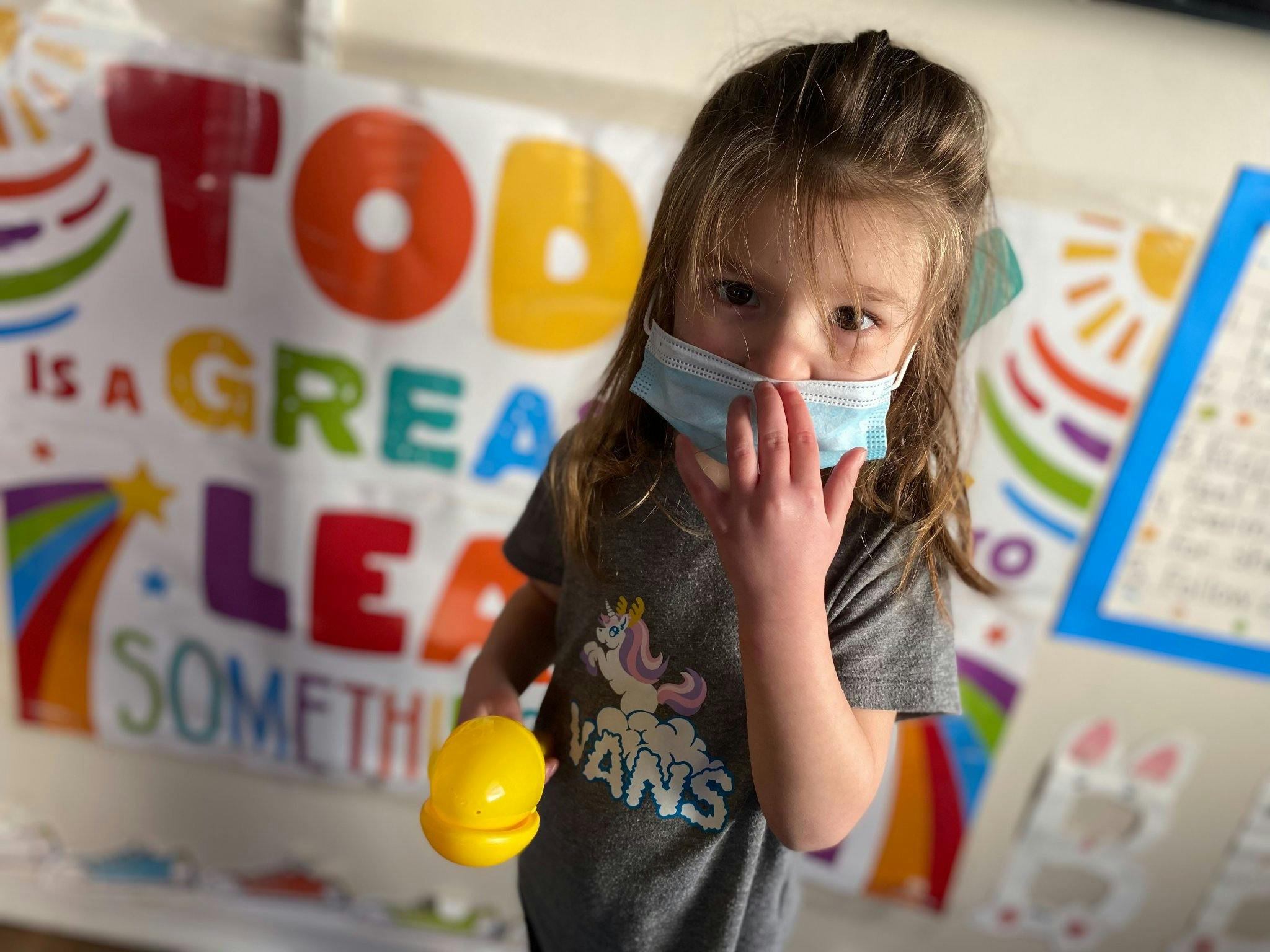 Child wearing a face mask and holding a yellow toy