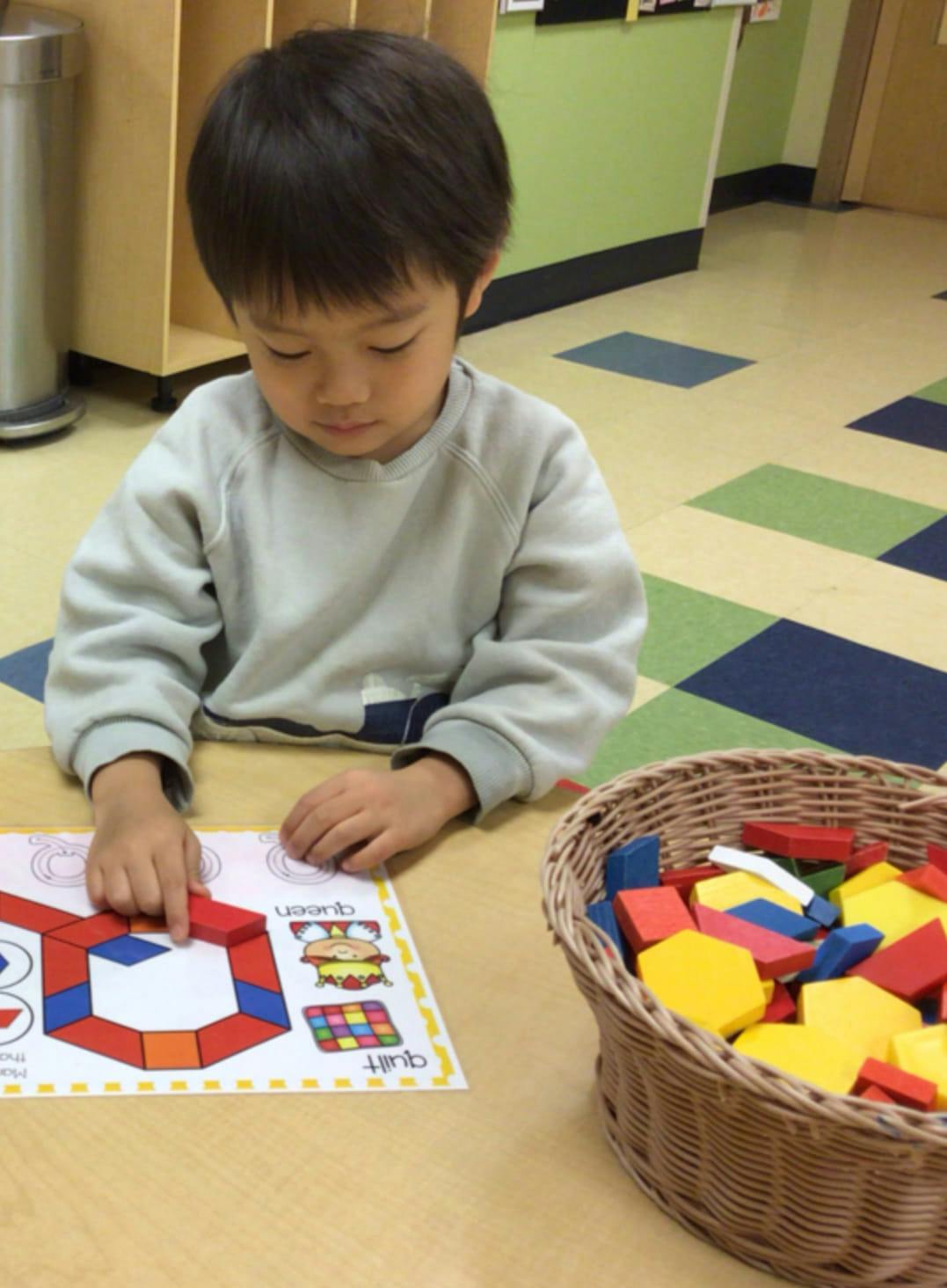 Child playing with colorful geometric blocks on a pattern sheet with a pattern card