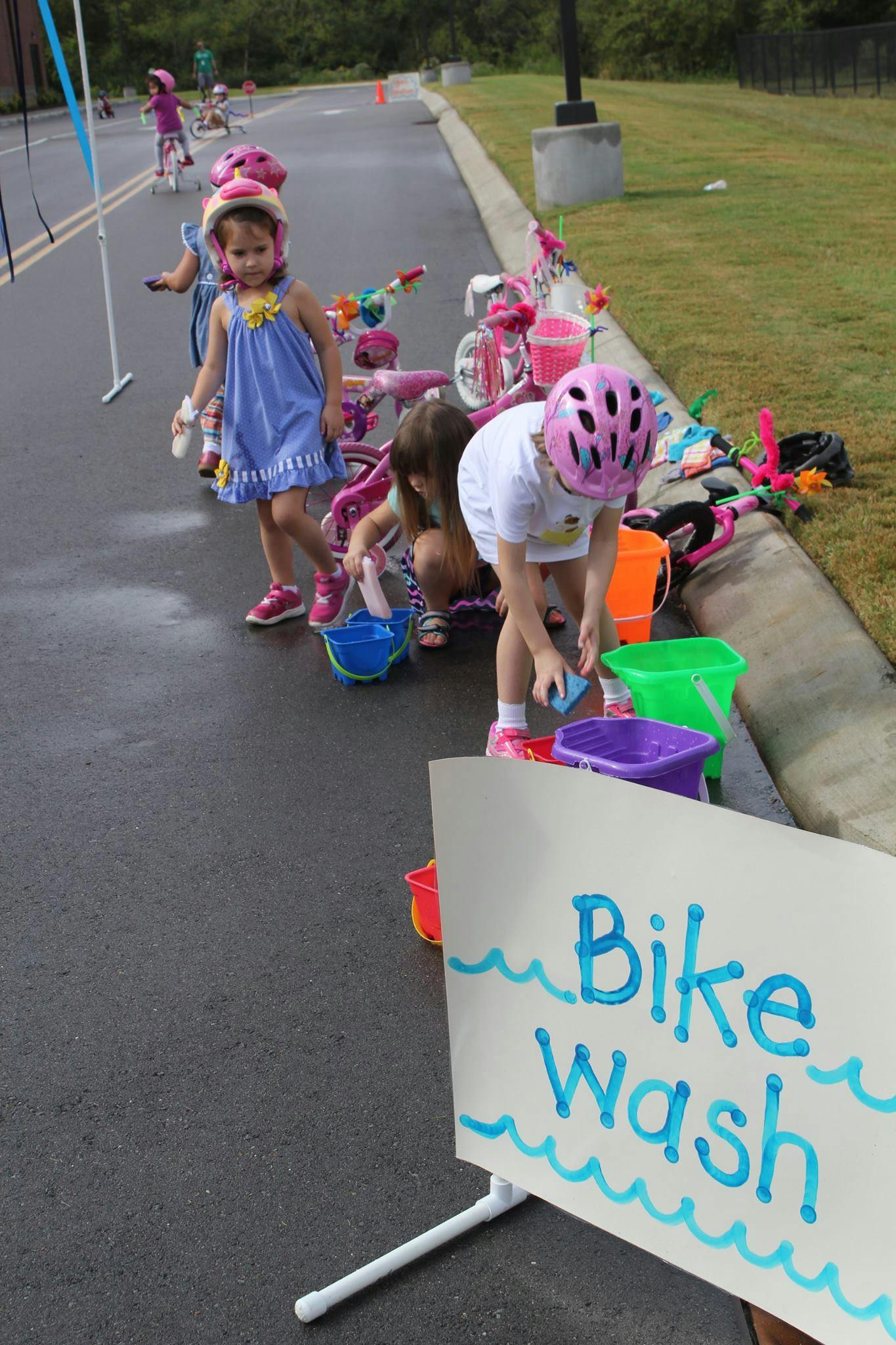 Children with helmets and bikes at a "Bike Wash" stand