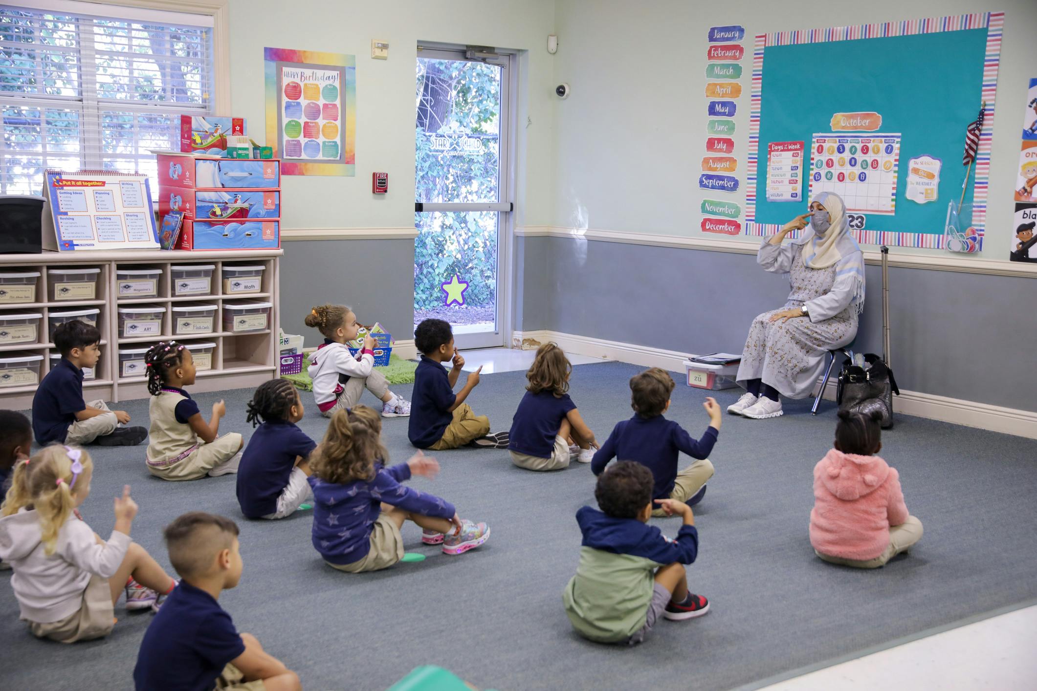 Adult sitting in a chair with children sitting on the floor in a classroom