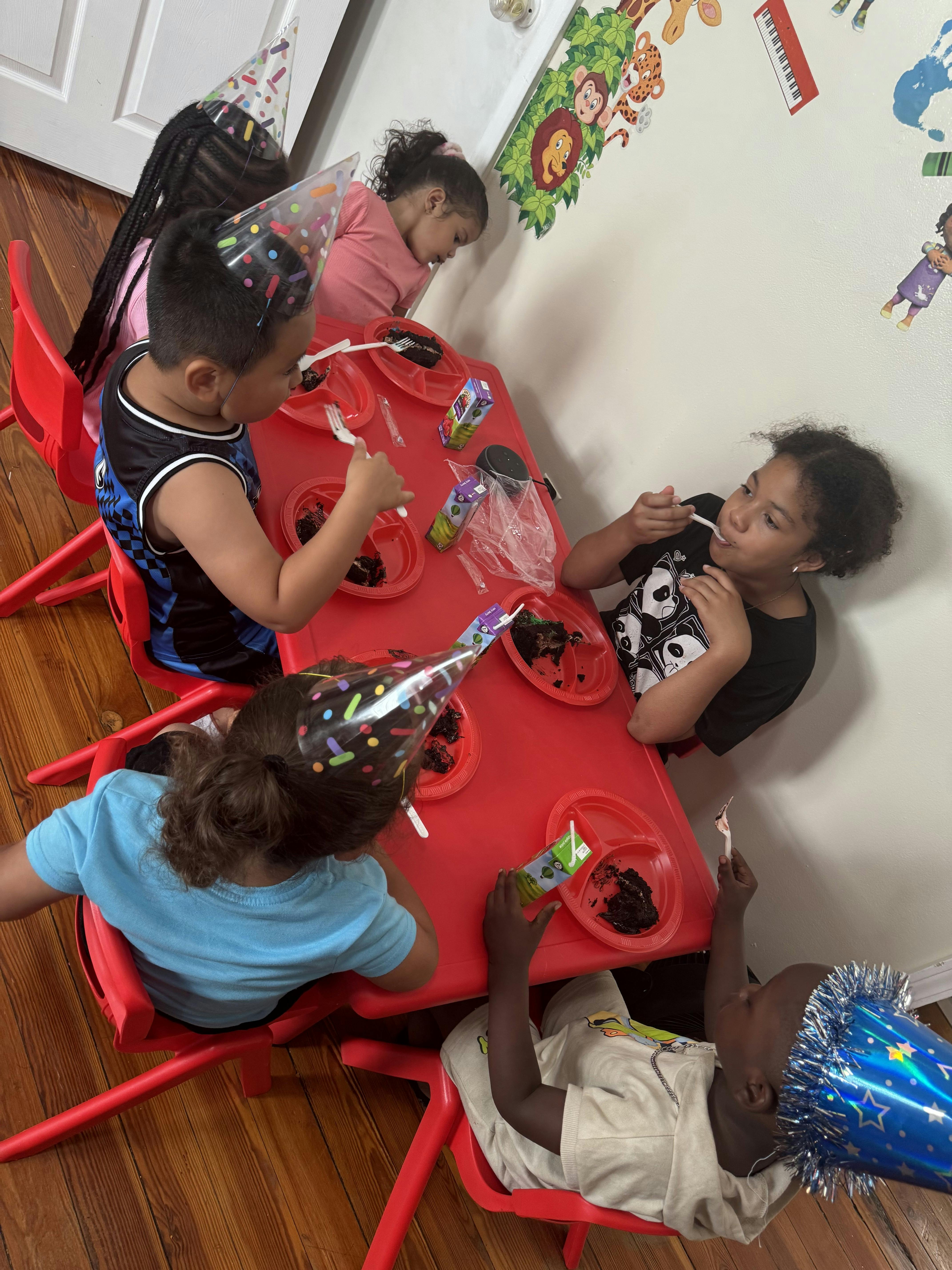 Children wearing party hats eating at a red table