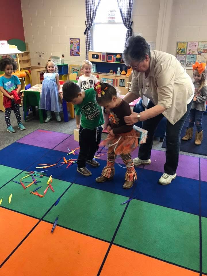 Adult helping two children with an activity on a colorful mat in a classroom