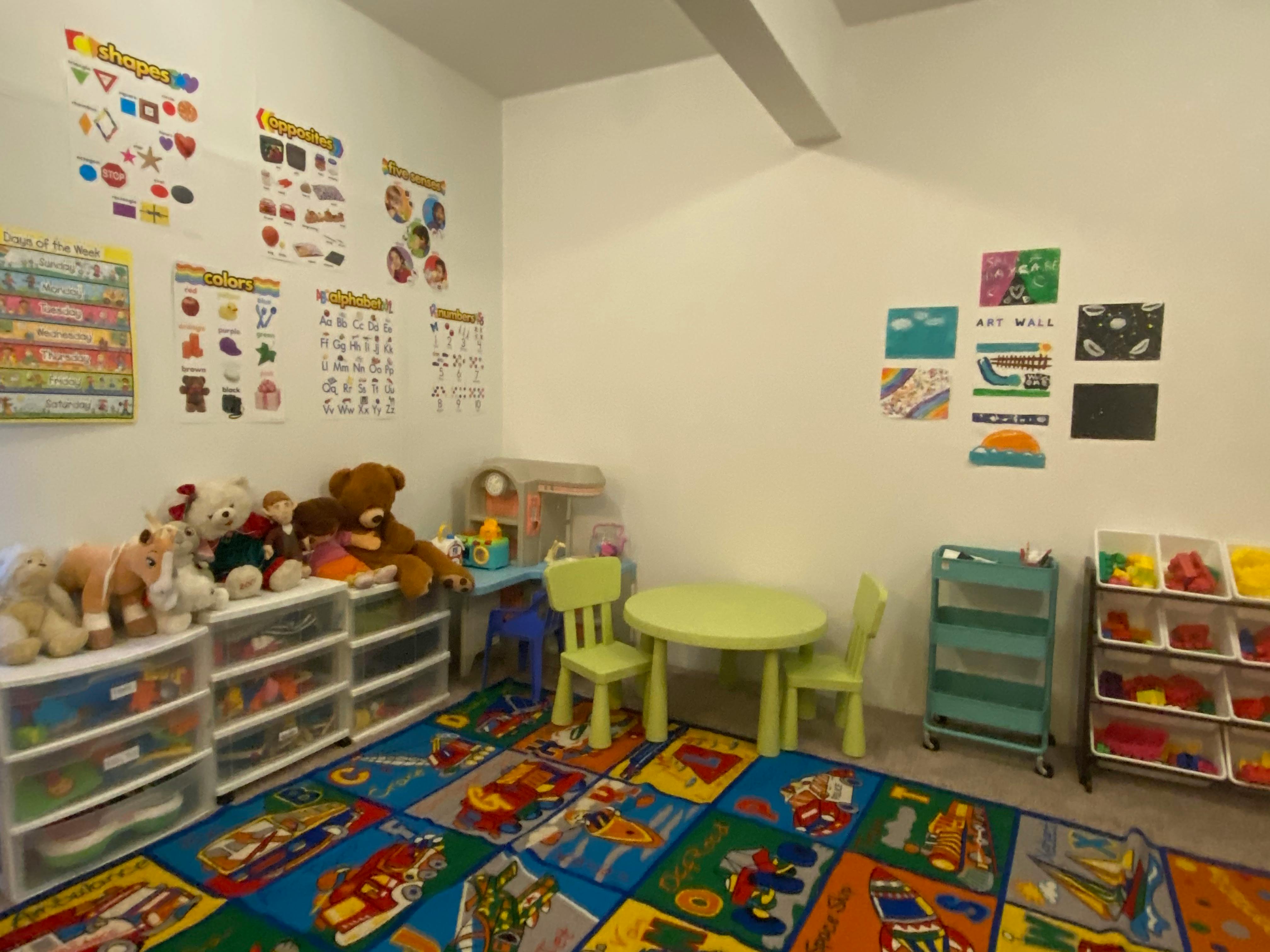 Playroom with colorful rug, small table and chairs, toys, and educational posters