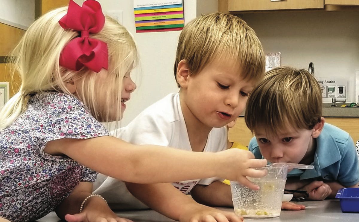 Three children looking at a container with a straw