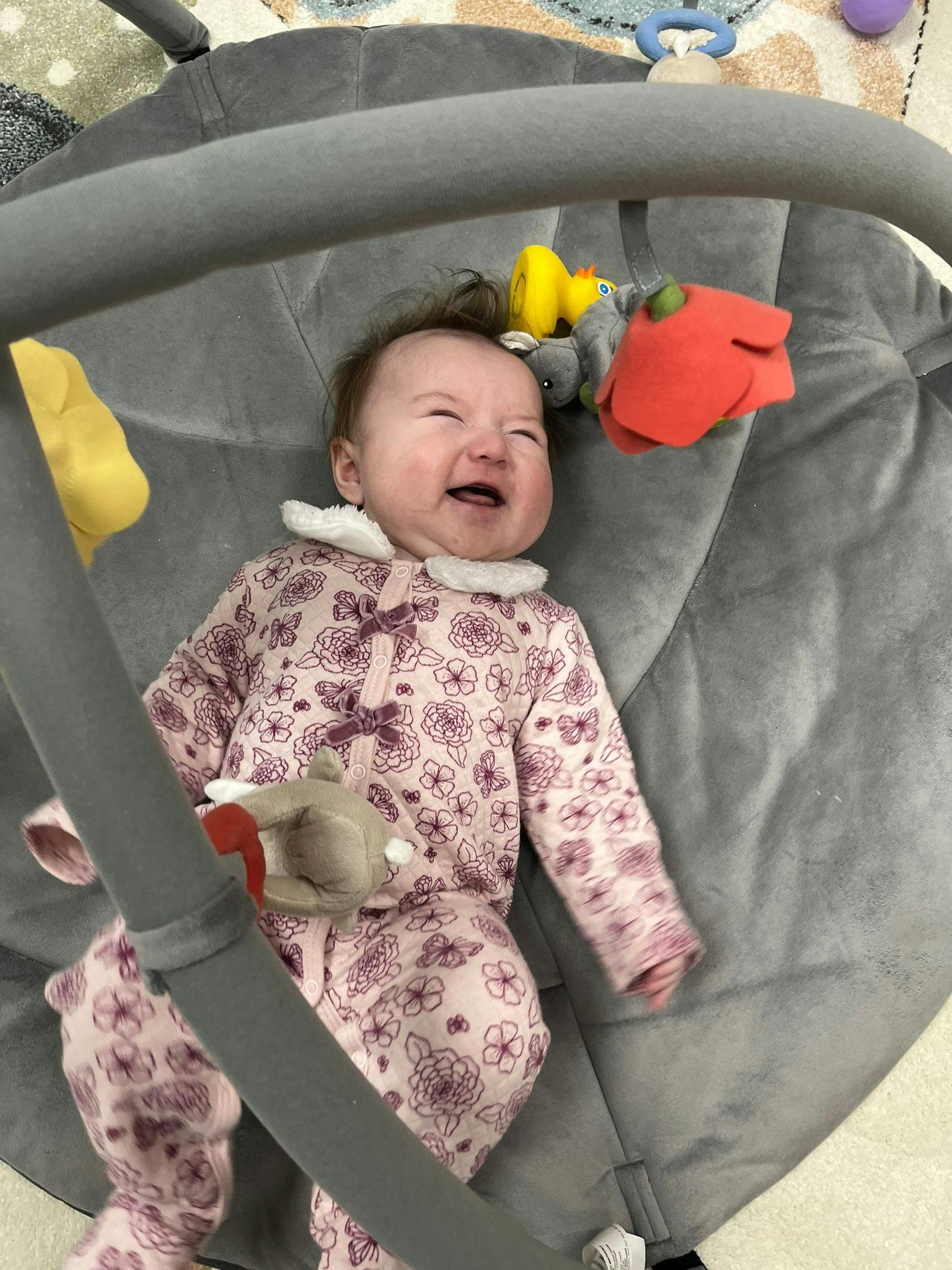 Child in a floral onesie lying in a baby bouncer with toys
