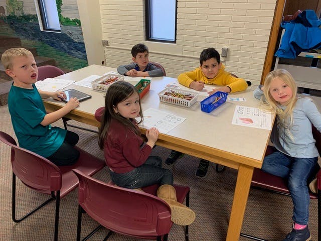 Five children sitting around a table with papers and supplies