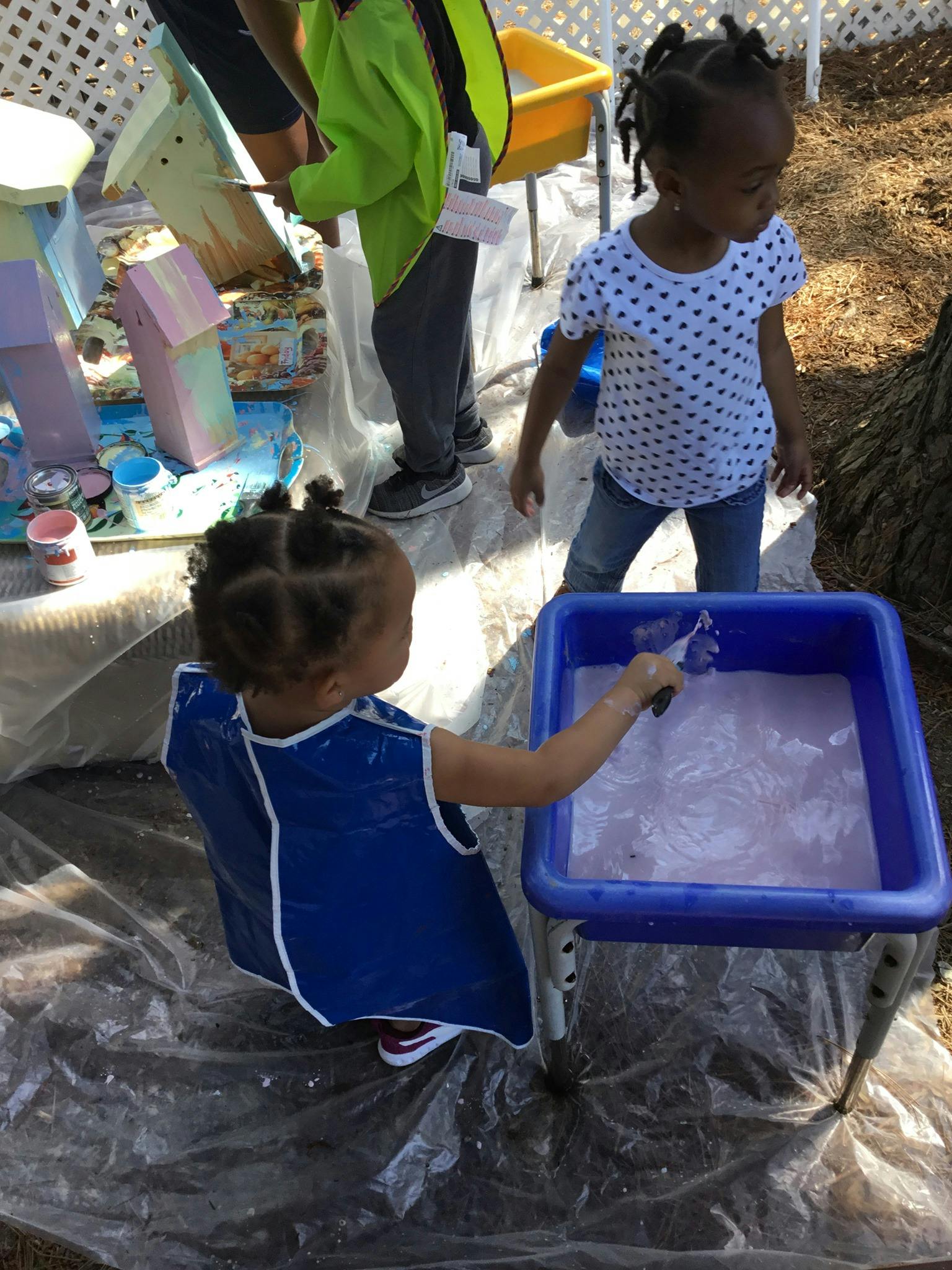 Child in blue smock playing with water in a blue bin