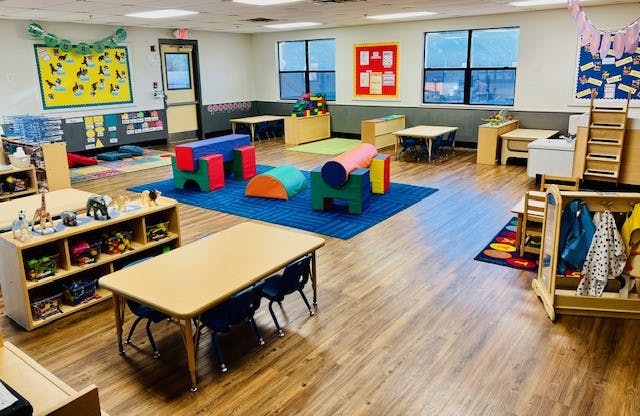 An empty classroom with small tables, chairs, and play equipment