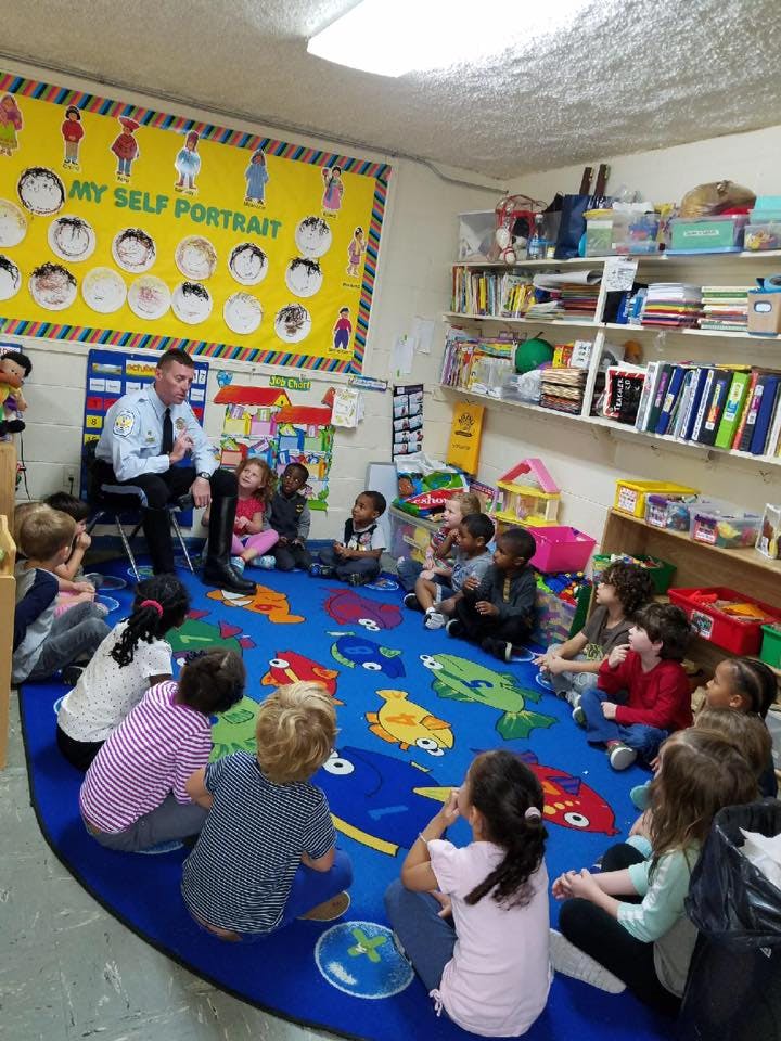 Person in uniform speaking to a group of children sitting on a rug