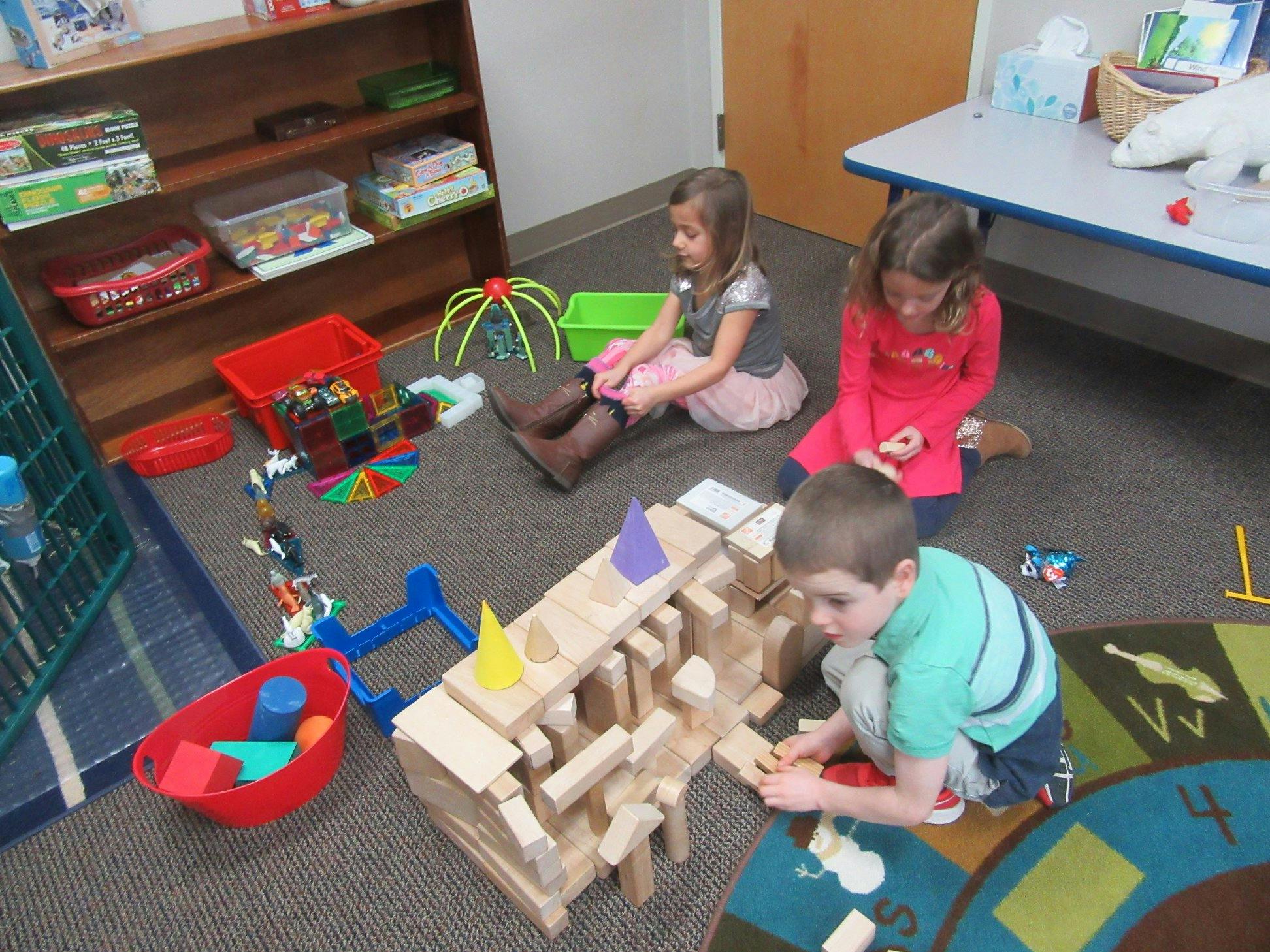 Three children playing with wooden blocks on a rug