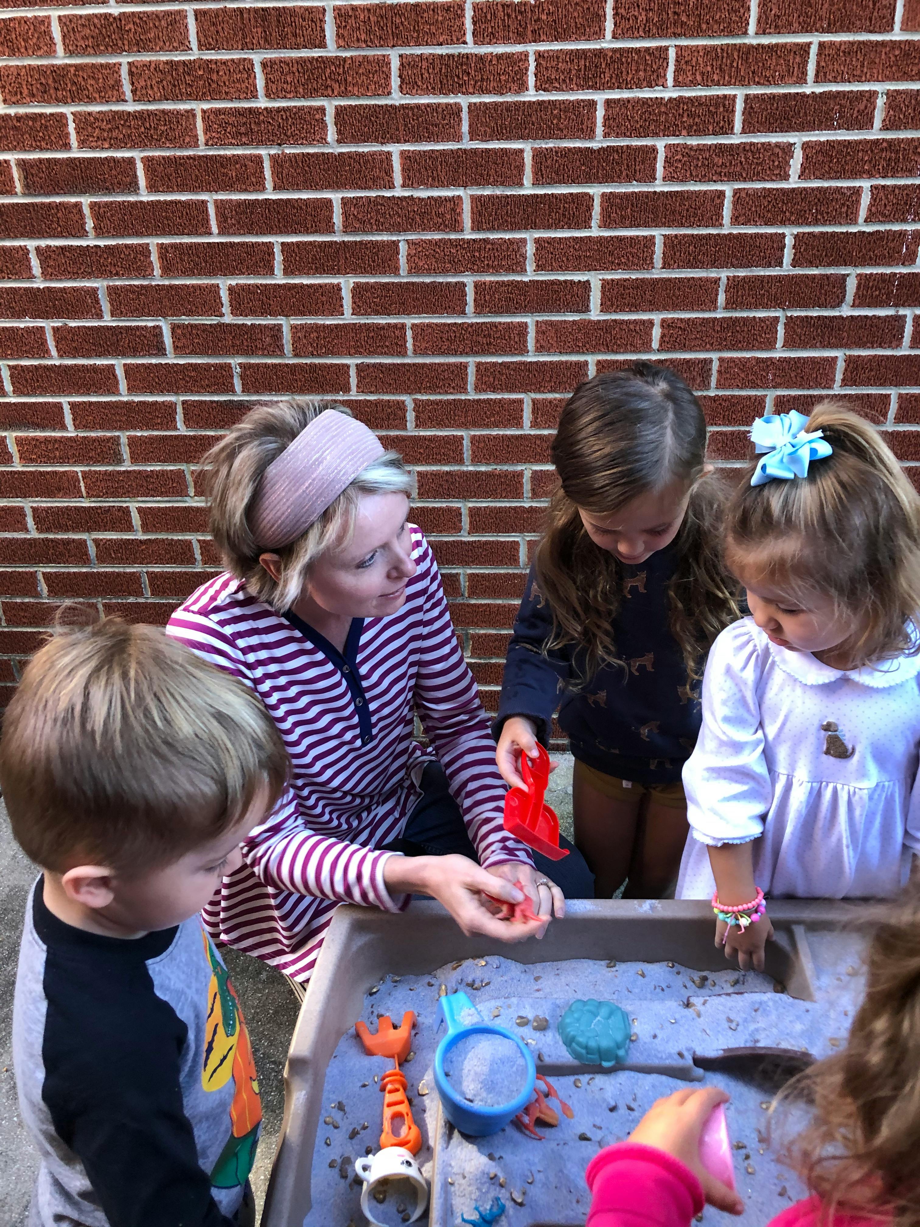 Adult and three children playing with sand and toys in a sand table