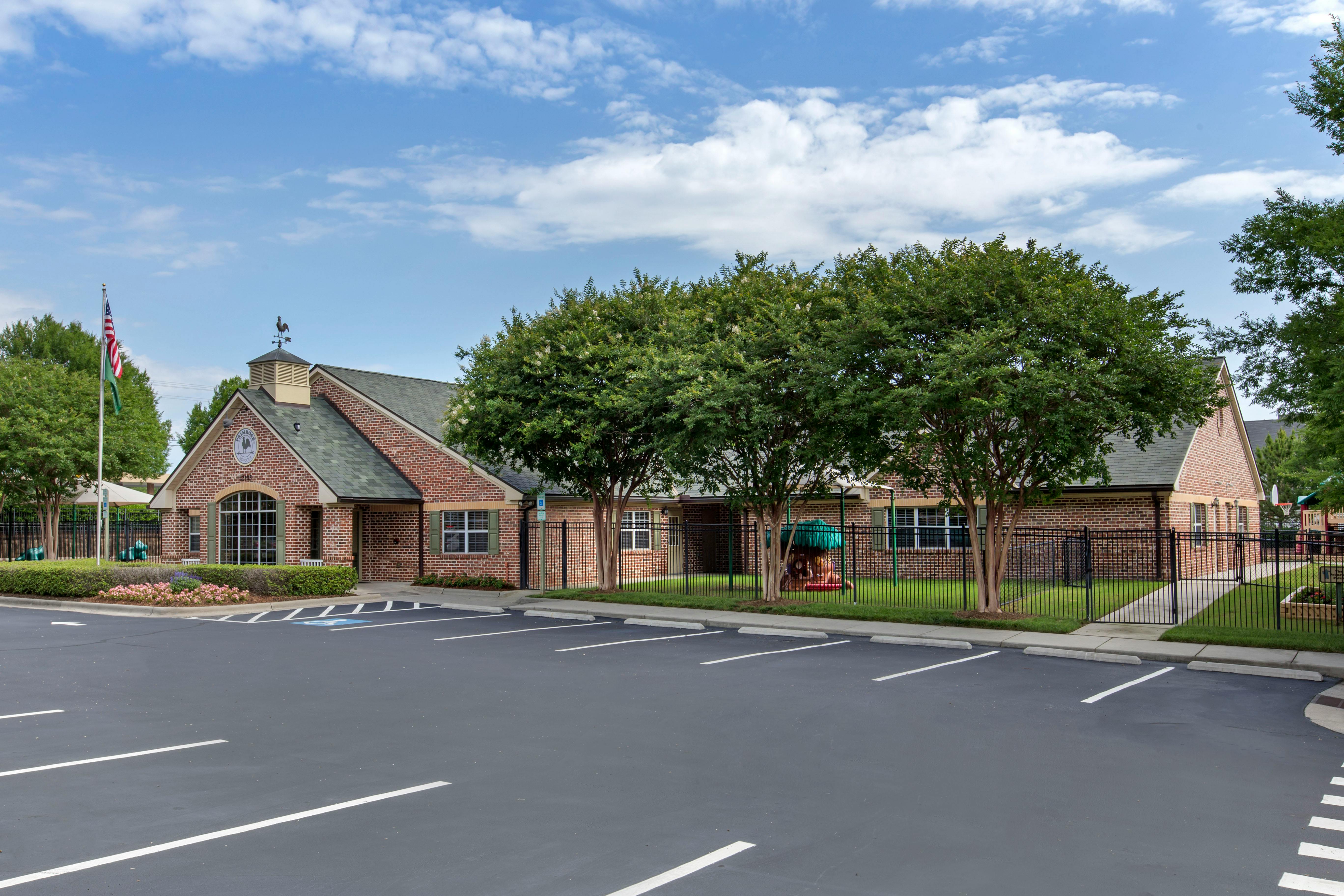 Brick building with a parking lot in front and a playground area behind a fence
