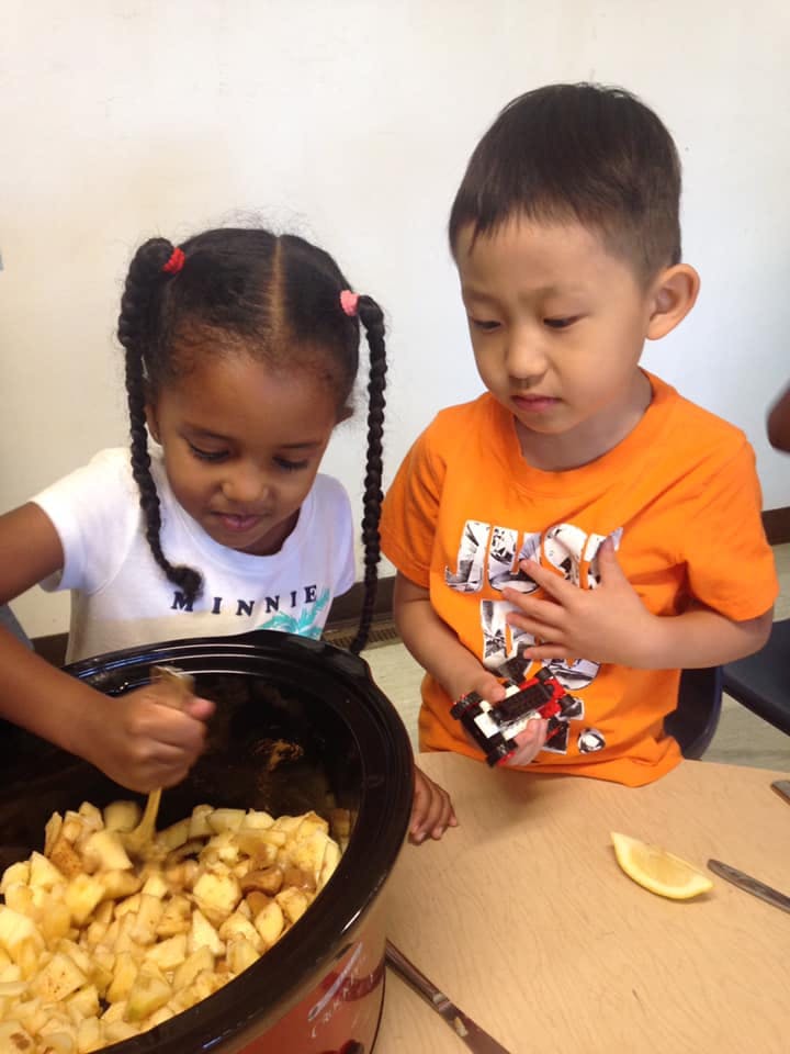 Child stirring food in a pot next to another child