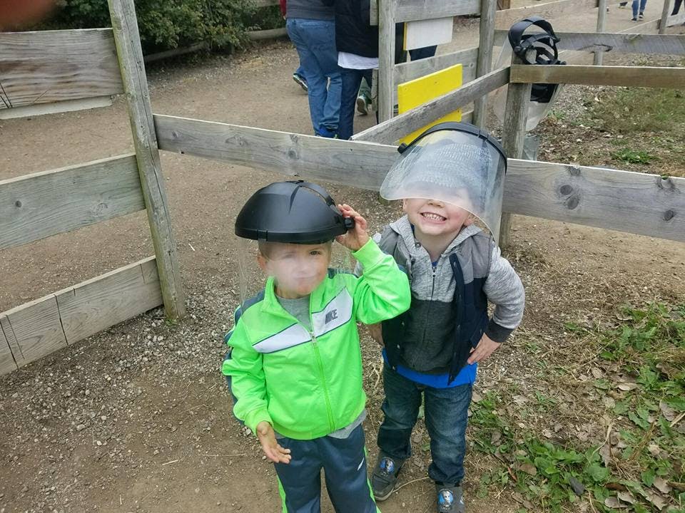 Two children wearing protective headgear standing near a wooden fence