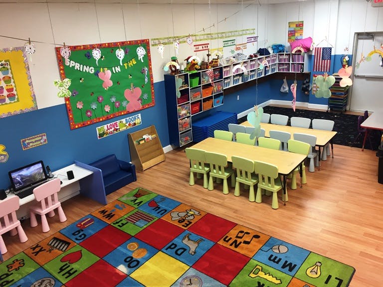 Classroom with small tables and chairs, a colorful alphabet rug, and wall decorations