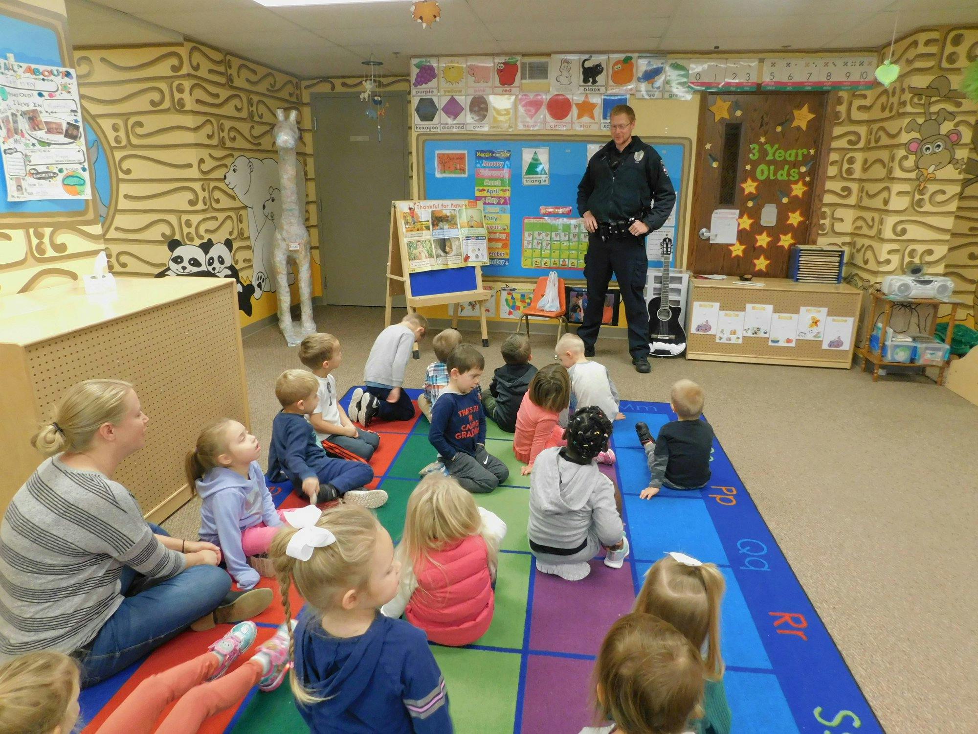 Police officer standing in front of children and an adult sitting on a rug