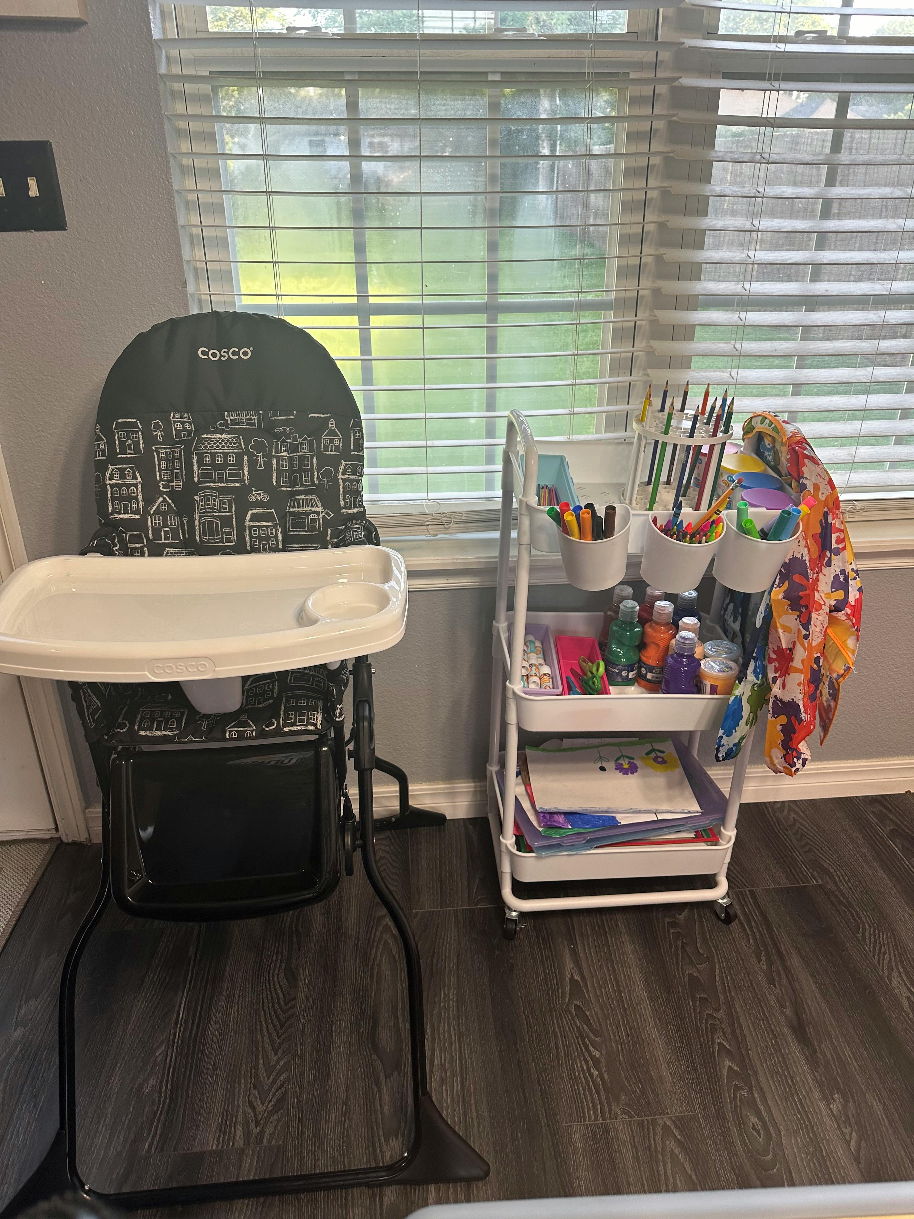 High chair with a white tray next to a rolling cart with art supplies