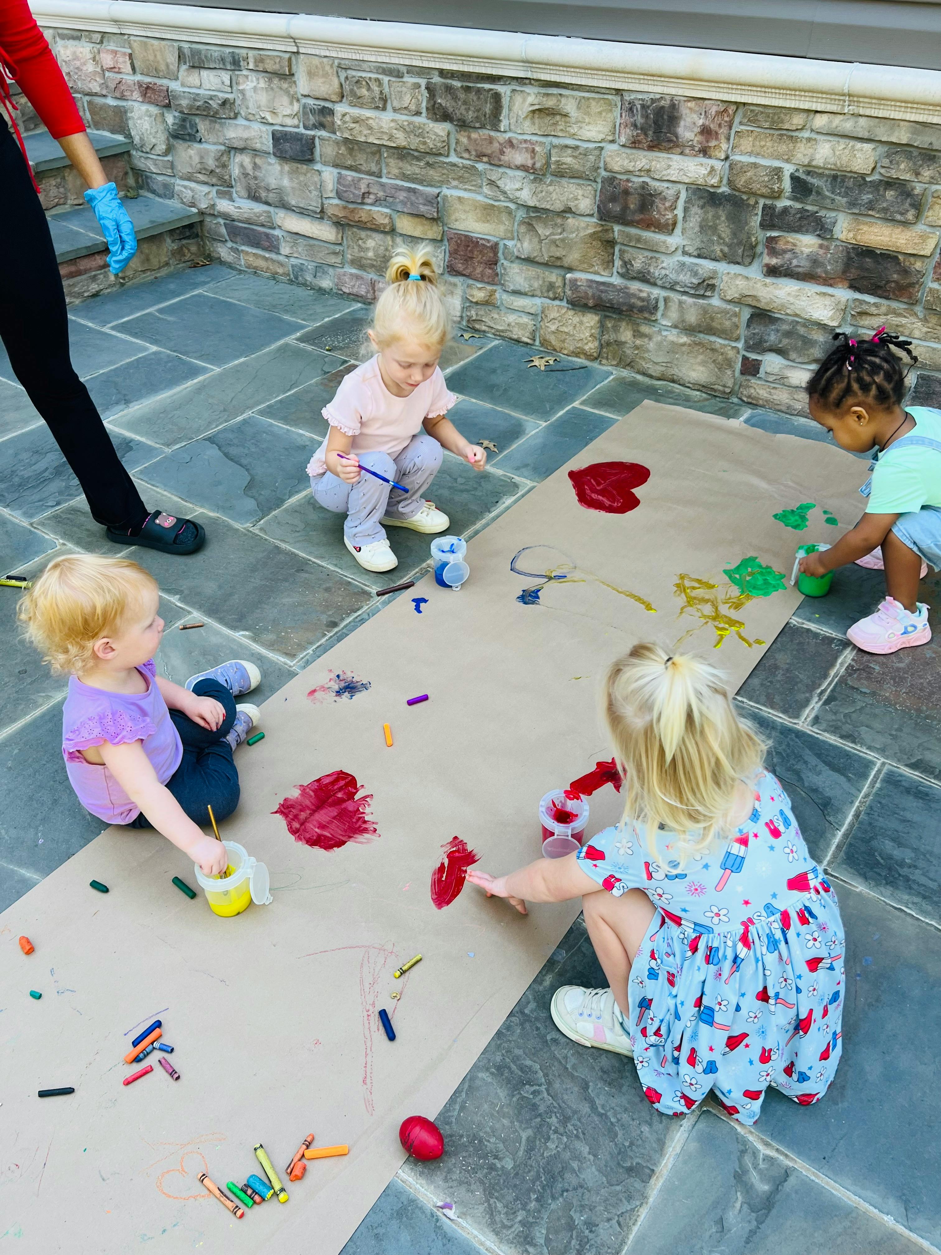 Children painting and drawing on a large sheet of paper outdoors