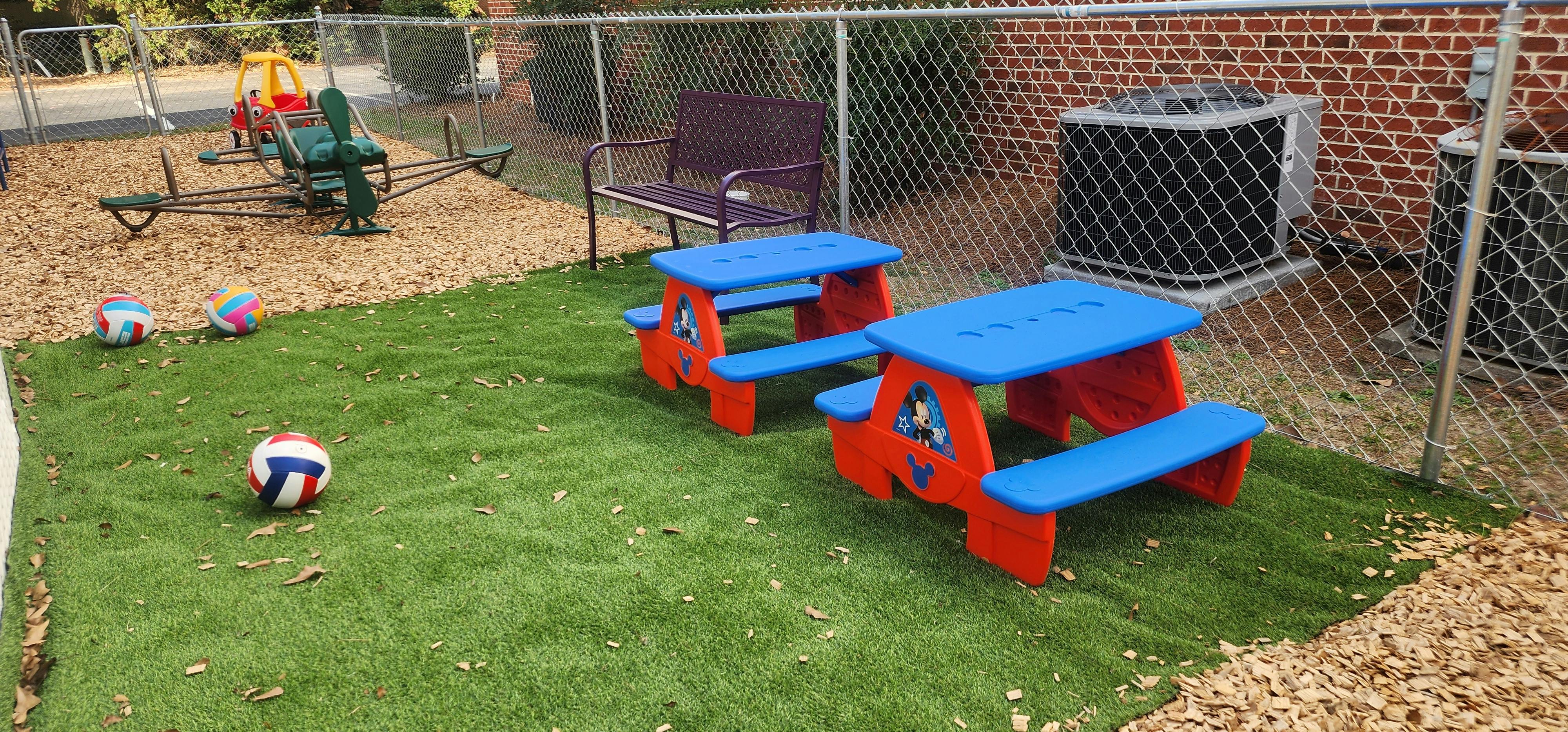 Children's playground with small picnic tables, balls, and a seesaw