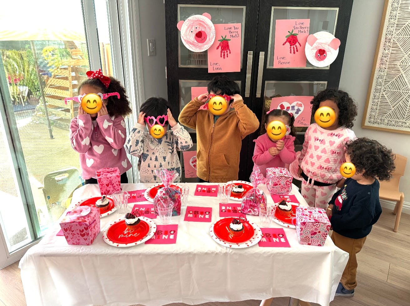 Children standing around a table set with red and pink party supplies