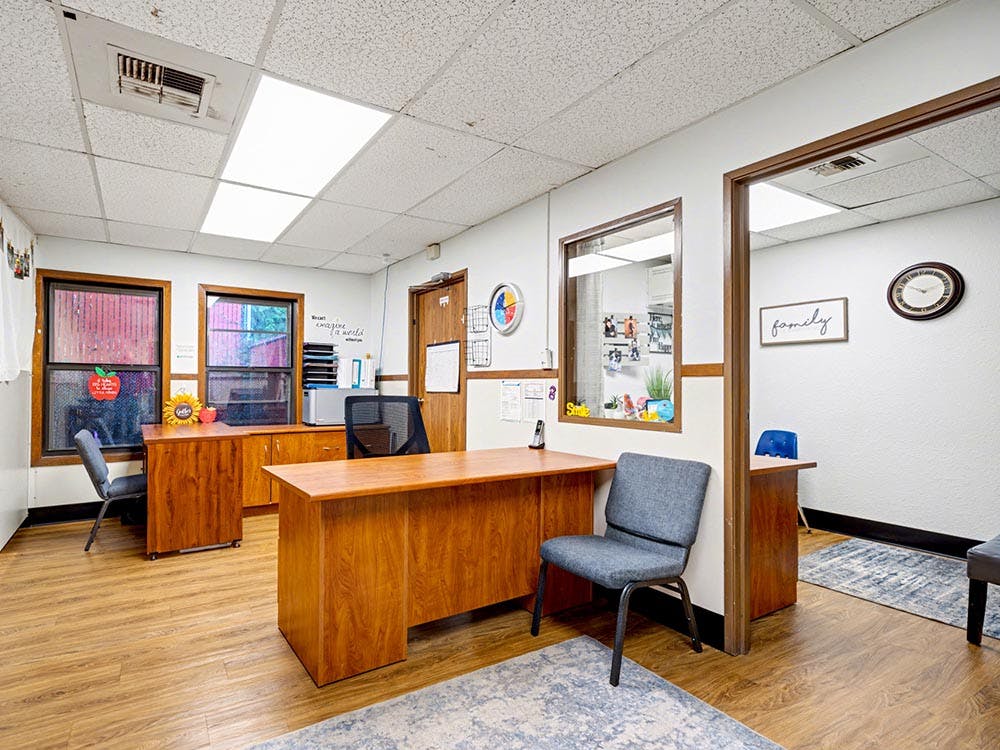 Reception area with wooden desks, two chairs, and a window looking into another room