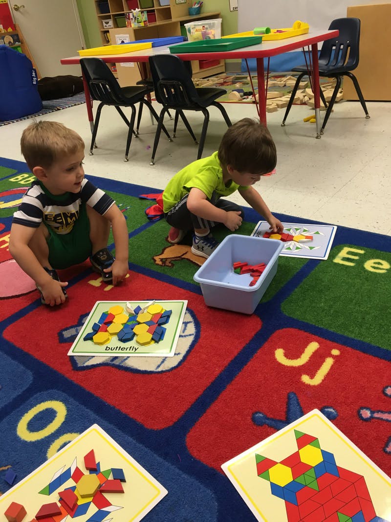 Two children playing with pattern blocks on a rug