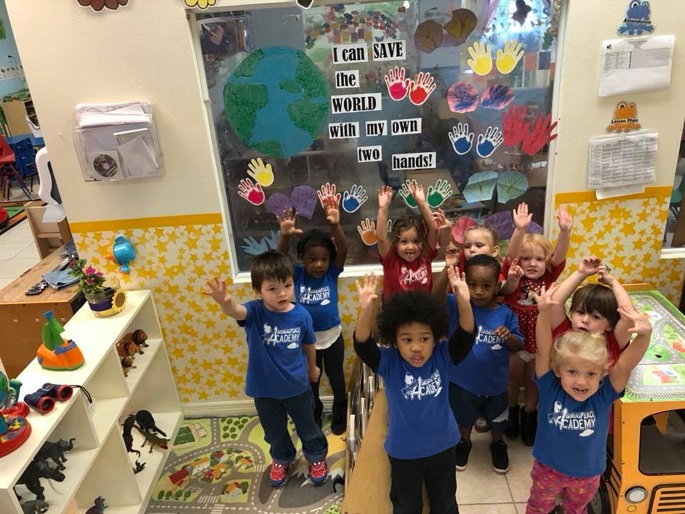 Group of children in blue shirts raising their hands in a classroom
