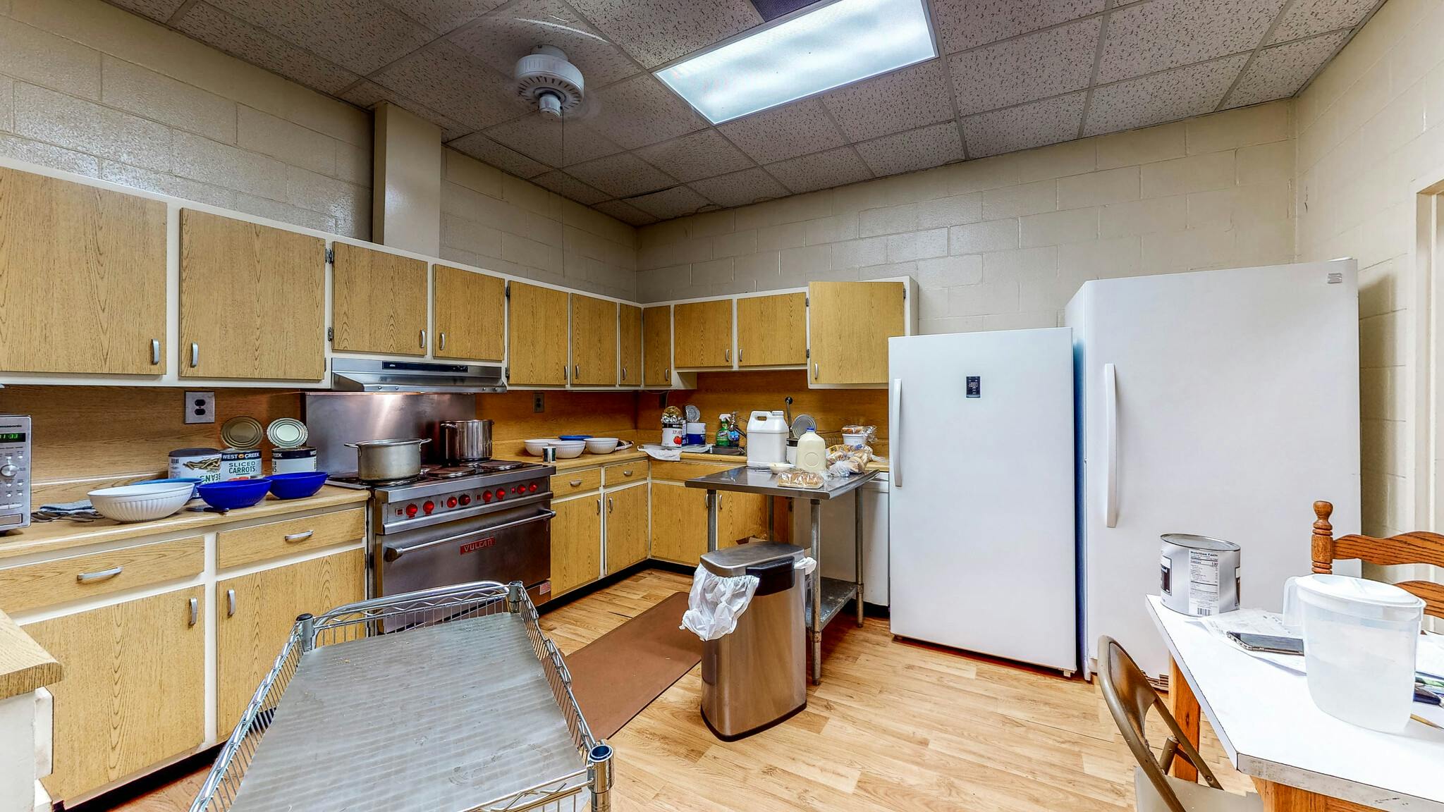 A commercial kitchen with wooden cabinets, stainless steel appliances, and two white refrigerators