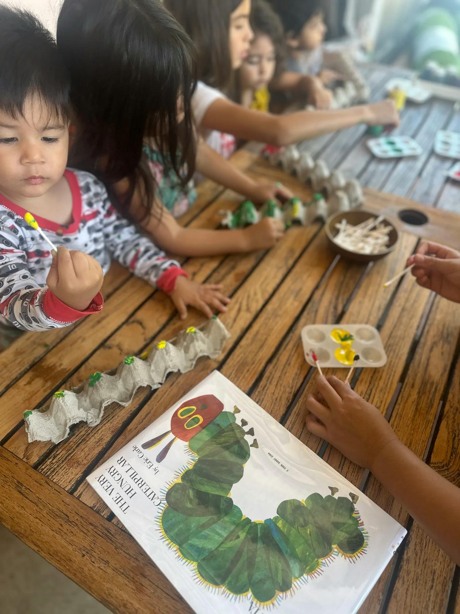 Children painting egg cartons at a table with a book on the table