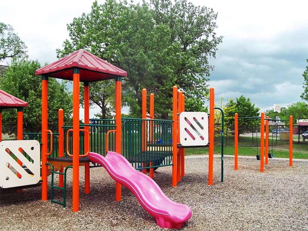 Playground with a pink slide, orange poles, and red roofs under a cloudy sky