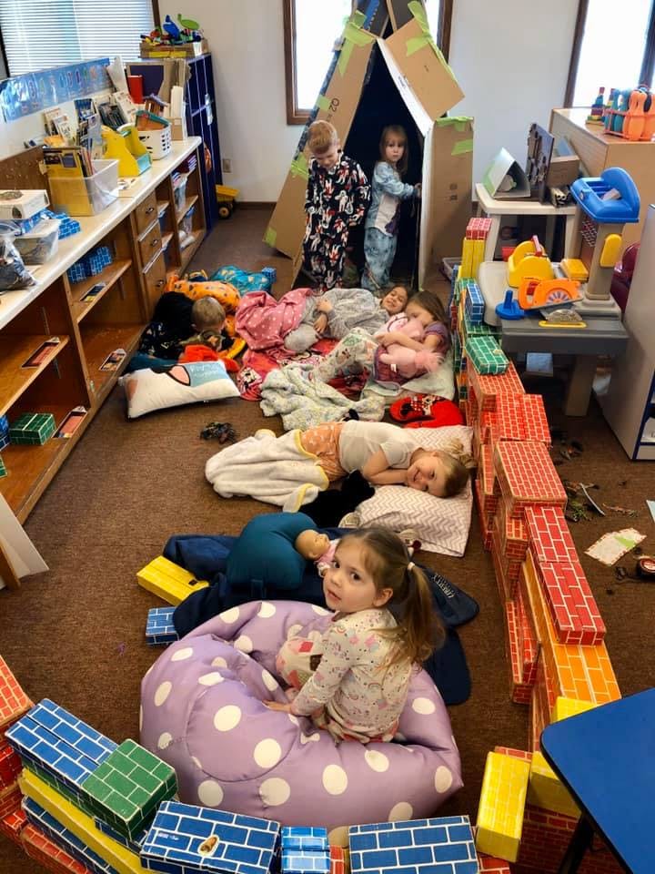 Children playing and resting on the floor in a room with a cardboard fort
