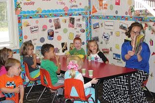 Adult reading to children at a table in a classroom